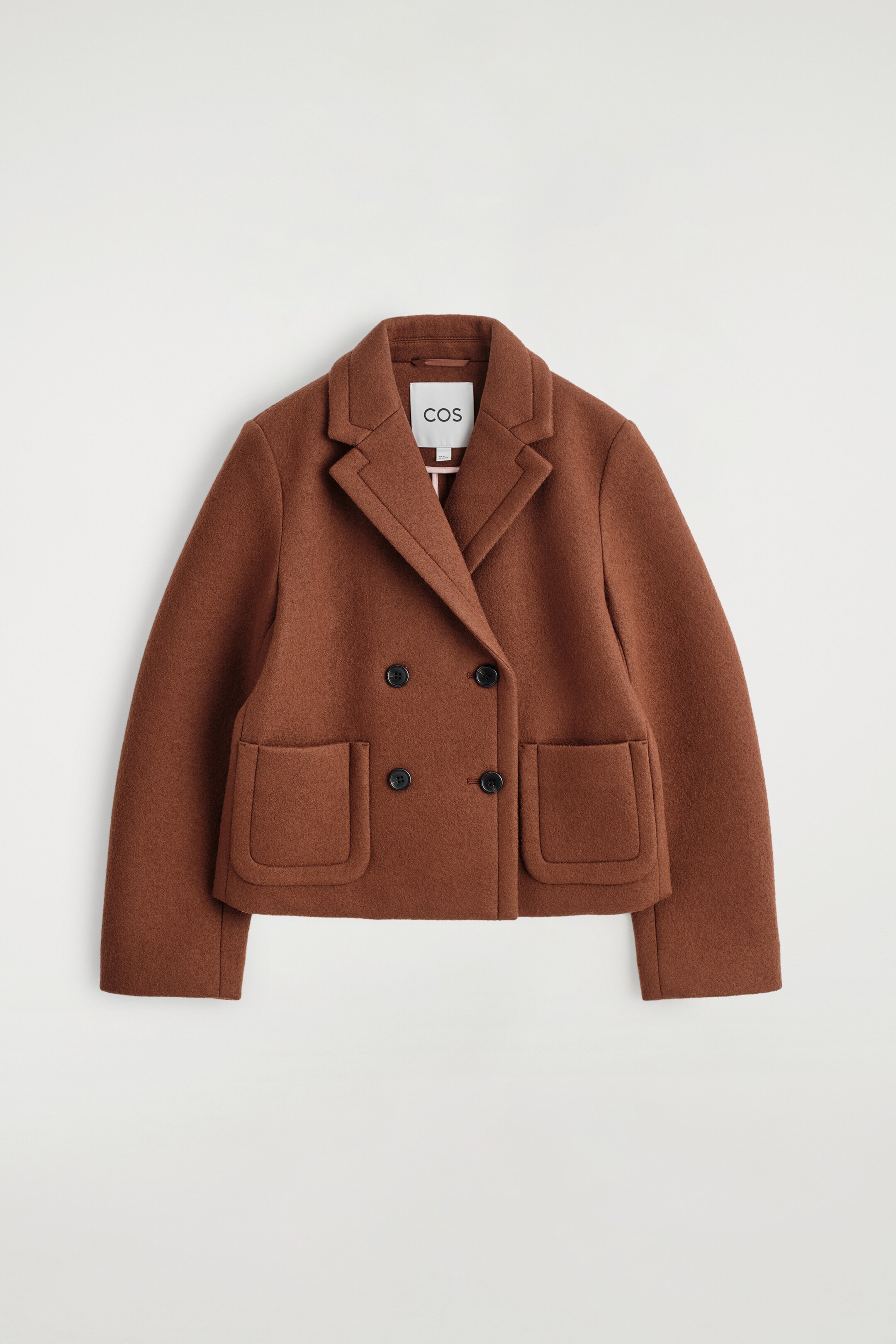 View larger image: A rust brown double-breasted jacket is presented front-facing, featuring wide notch lapels and a double-breasted front closure with four black buttons. Two large, rounded patch pockets are visible near the jacket's cropped hem.