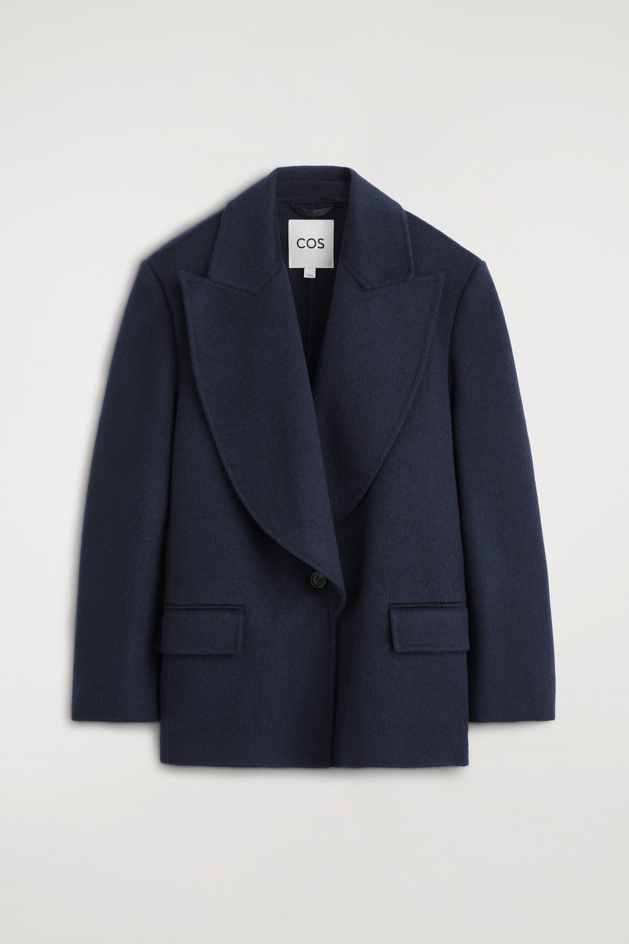 A navy blue wool-blend blazer is shown from the front, featuring wide, draped lapels and a single-breasted, one-button fastening. The blazer features a textured, double-faced finish and two front flap pockets.