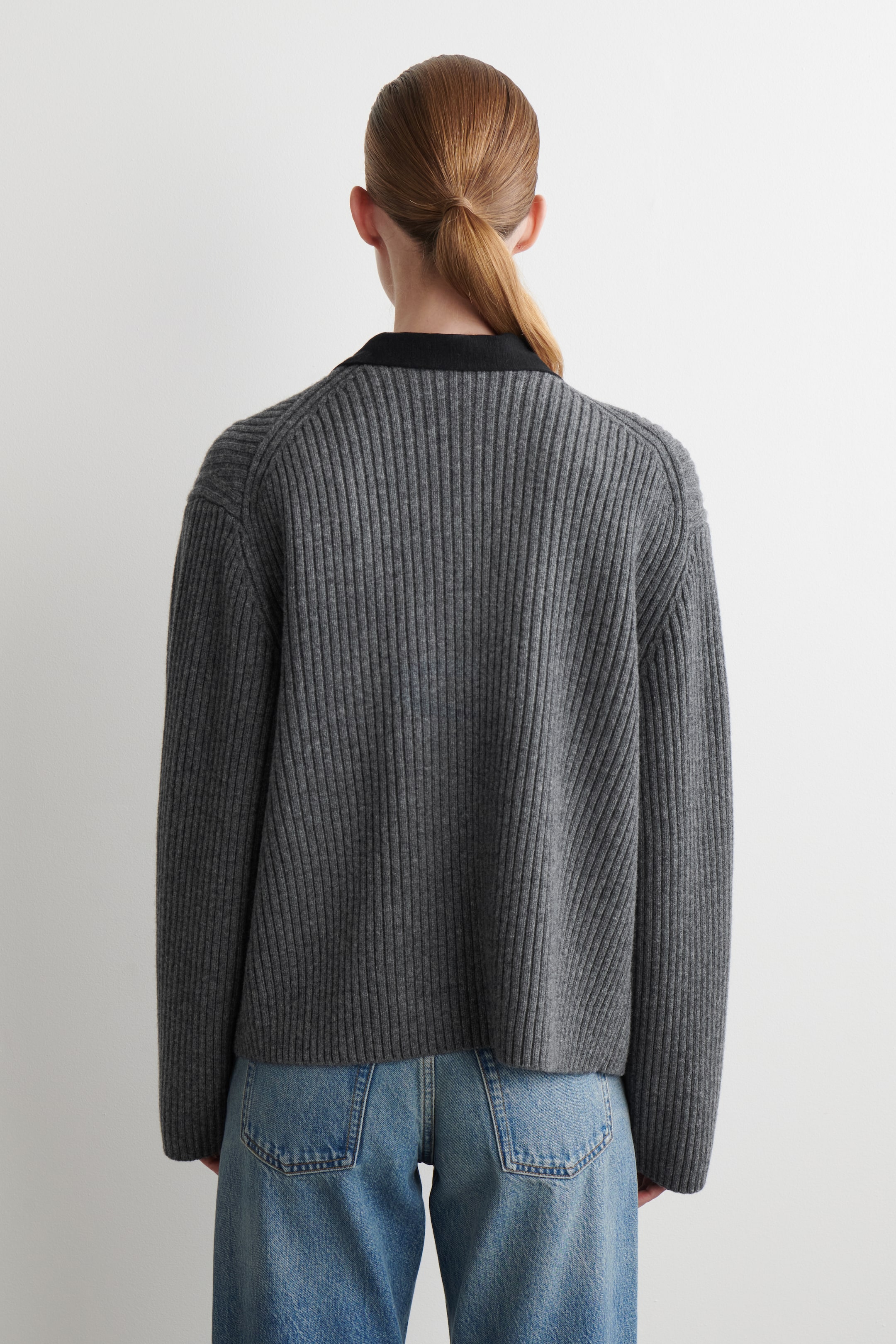 Visualizza immagine più grande: Un maglione a maglia a coste grigio scuro viene visto da dietro, caratterizzato da coste verticali prominenti, una vestibilità rilassata e un colletto nero a contrasto.