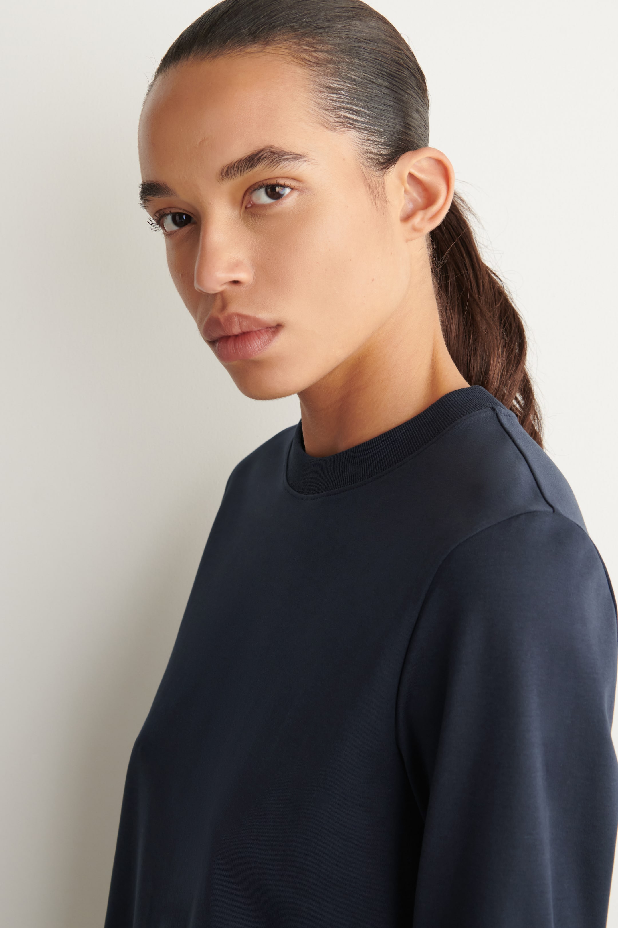View larger image: A dark blue long-sleeved top is being worn, showcasing its ribbed crew neck and smooth fabric. The garment fits smoothly across the shoulder and upper chest.
