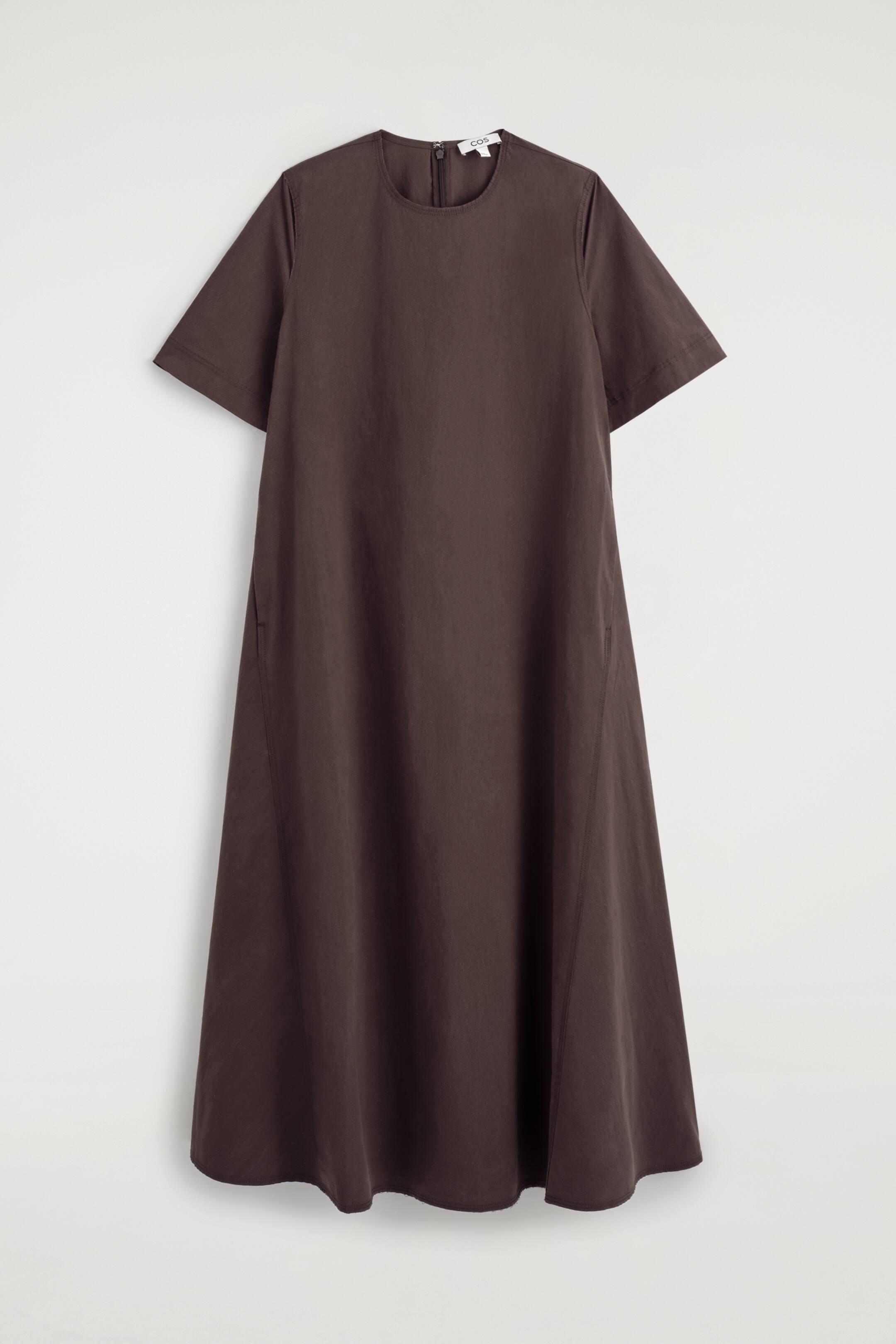 Grotere afbeelding bekijken: Een donkerbruine katoenen poplin T-shirt jurk wordt plat weergegeven, met de voorkant zichtbaar, korte mouwen, een ronde halslijn en een zichtbare ritssluiting aan de achterkant. De jurk heeft een A-lijn silhouet met zijnaadzakken, spiraalvormige naden en een onafgewerkte zoom.