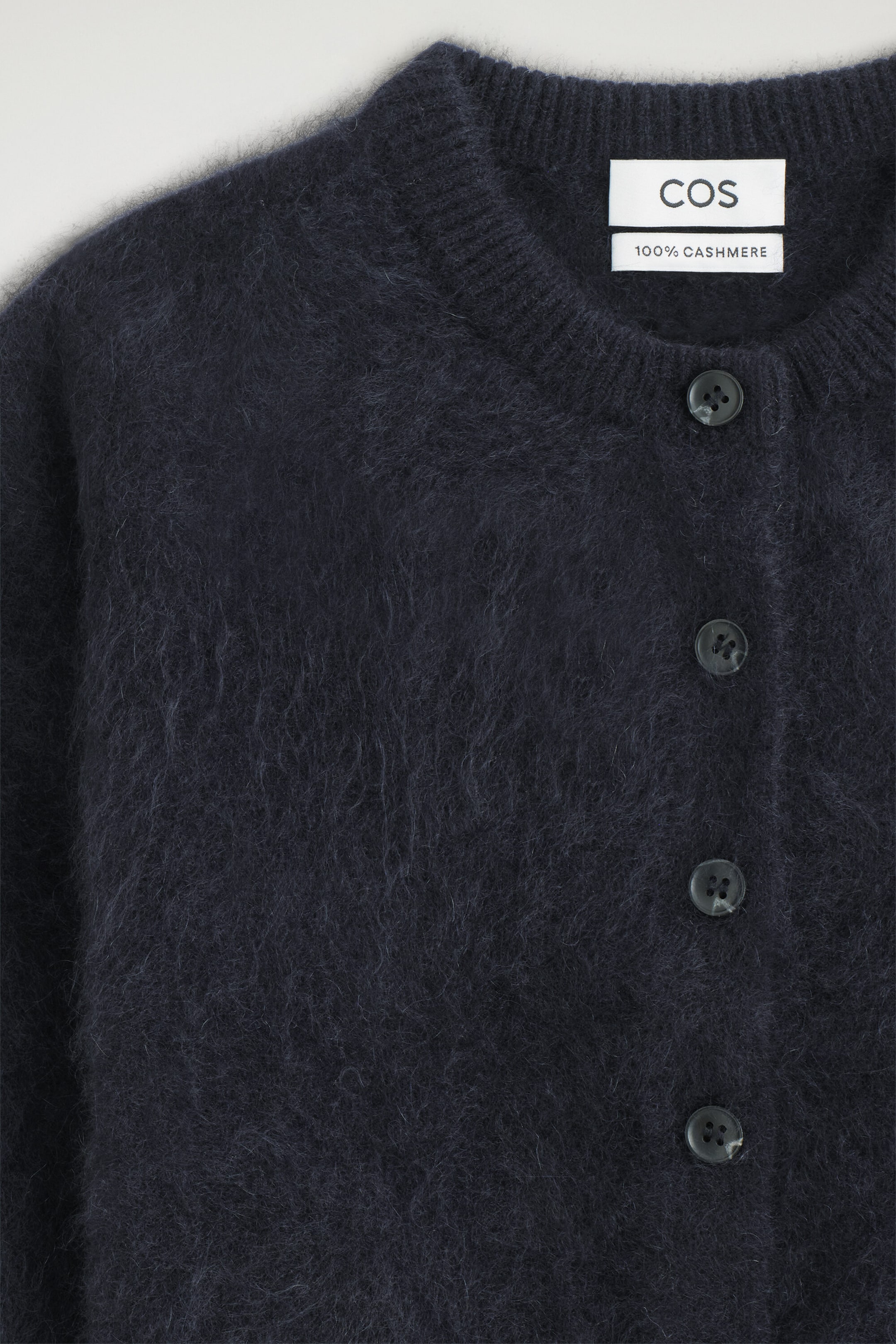 The kids' brushed pure cashmere cardigan is shown from the front in a soft, fuzzy texture in dark navy blue, highlighting its ribbed crew neck and button-front placket.