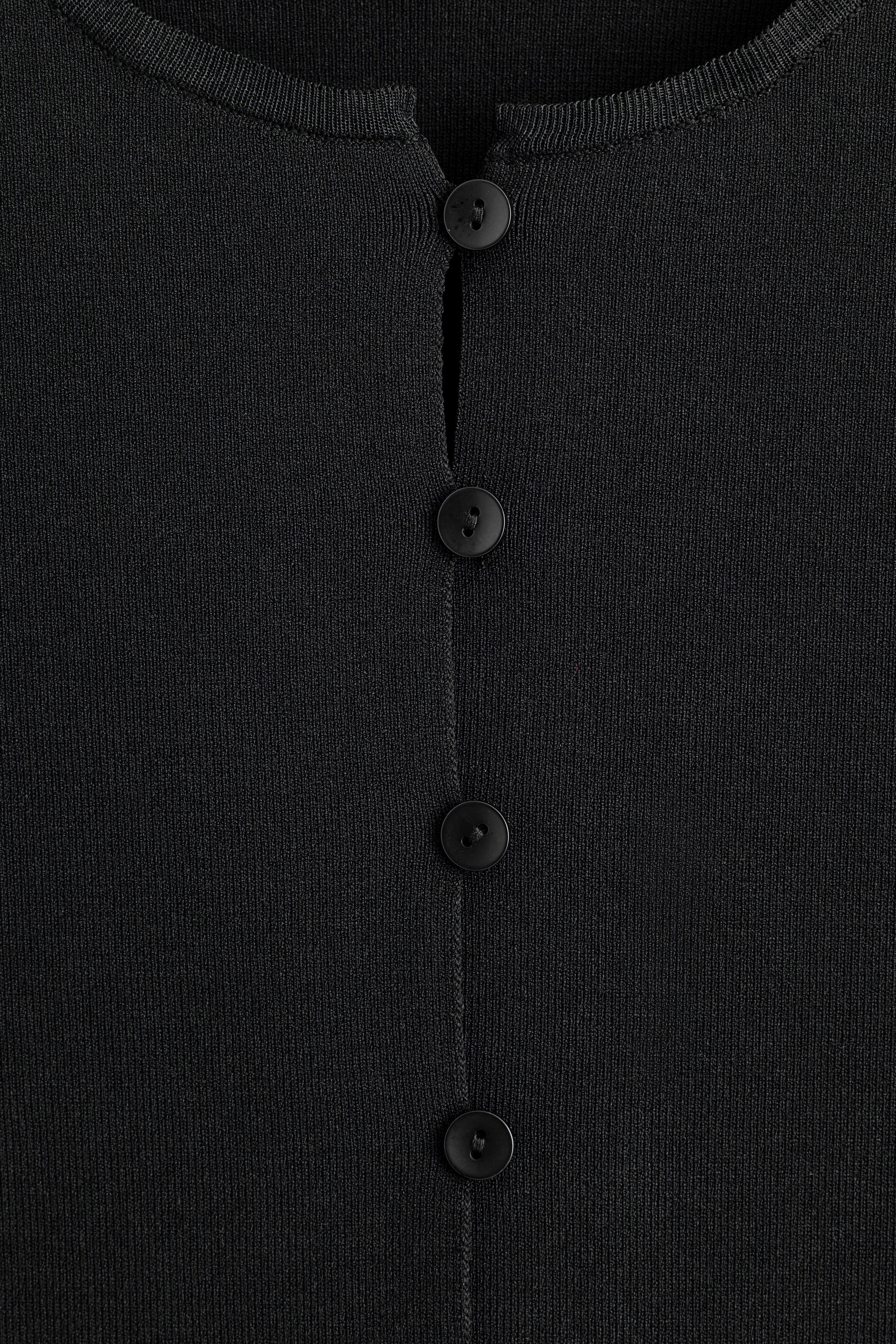 View larger image: A black fine-knit garment is presented as FRONT, featuring a ribbed round neckline and a central placket. Four black, round buttons are vertically aligned down the placket, with the top button unfastened.