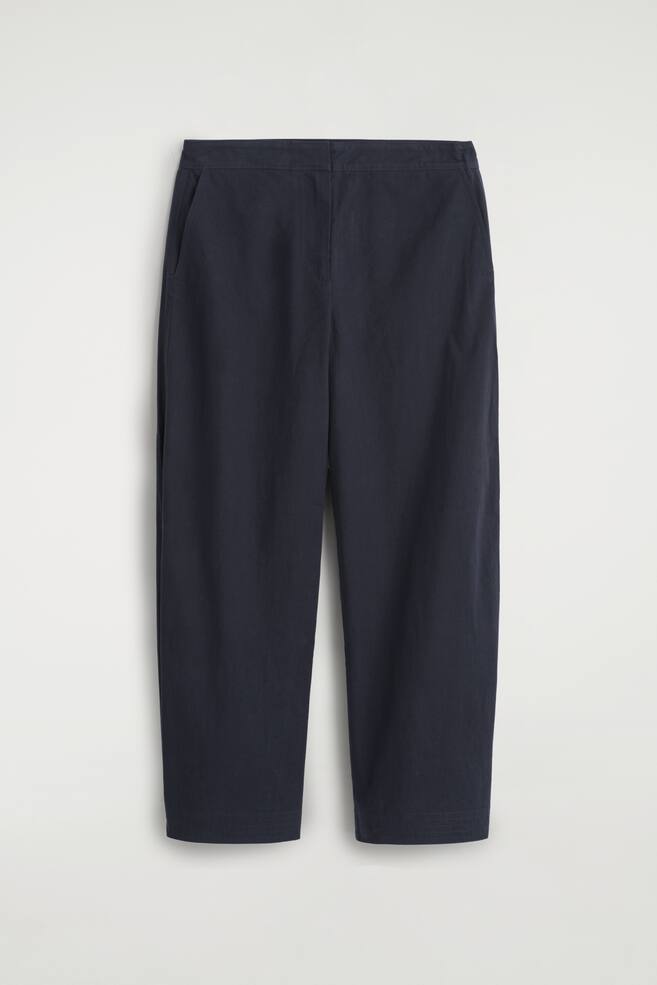 Ein Paar dunkelblaue Hosen wird von vorne gezeigt. Die Hosen verfügen über einen flachen Bund und offene Seitentaschen und präsentieren ein entspanntes, verkürztes Bein. - 1