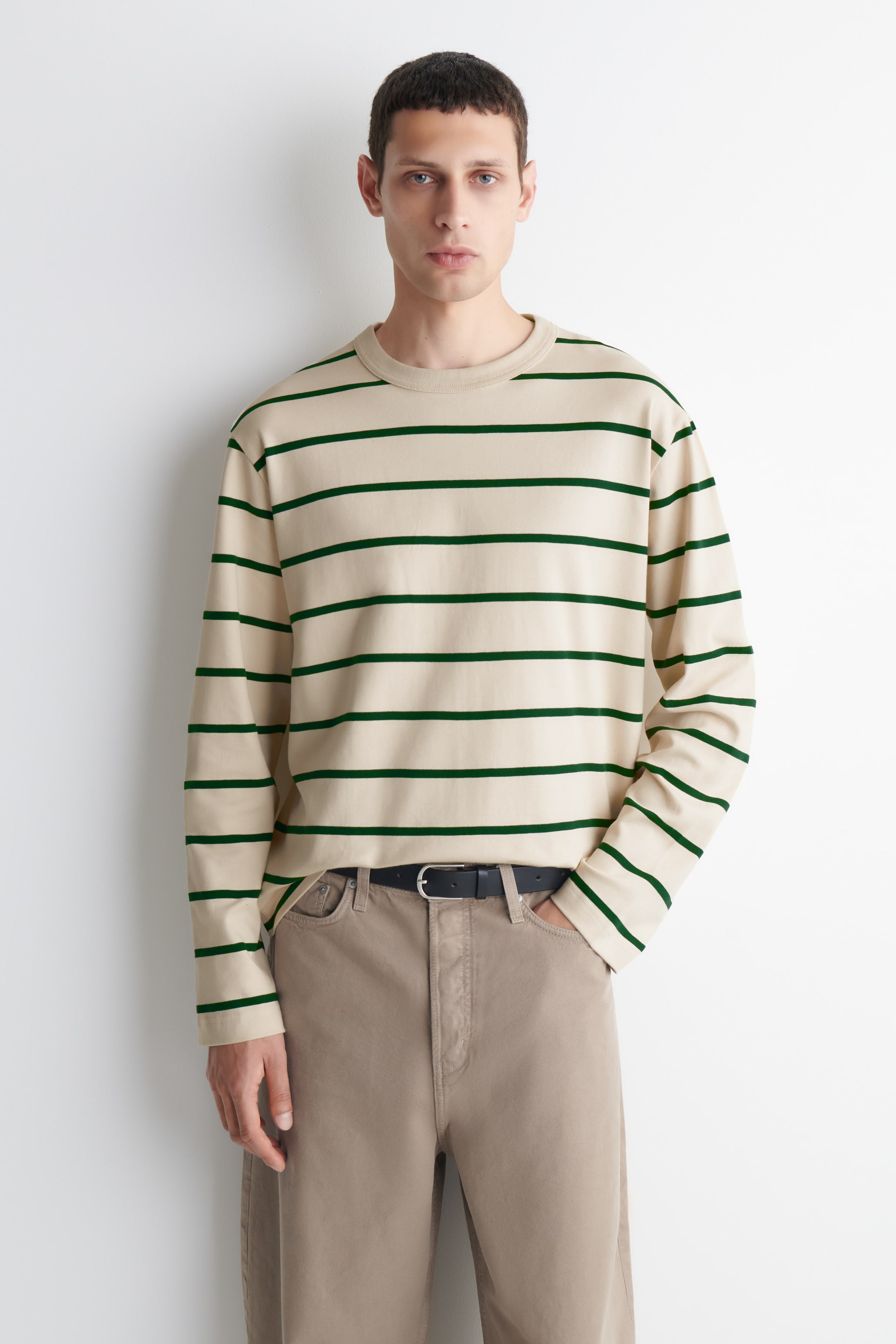 Grotere afbeelding bekijken: Een T-shirt met lange mouwen heeft een crèmekleurige achtergrond met donkergroene horizontale strepen. Het heeft een ribgebreide ronde hals en ribgebreide boorden en heeft een losse pasvorm, weergegeven vanuit een frontale hoek.
