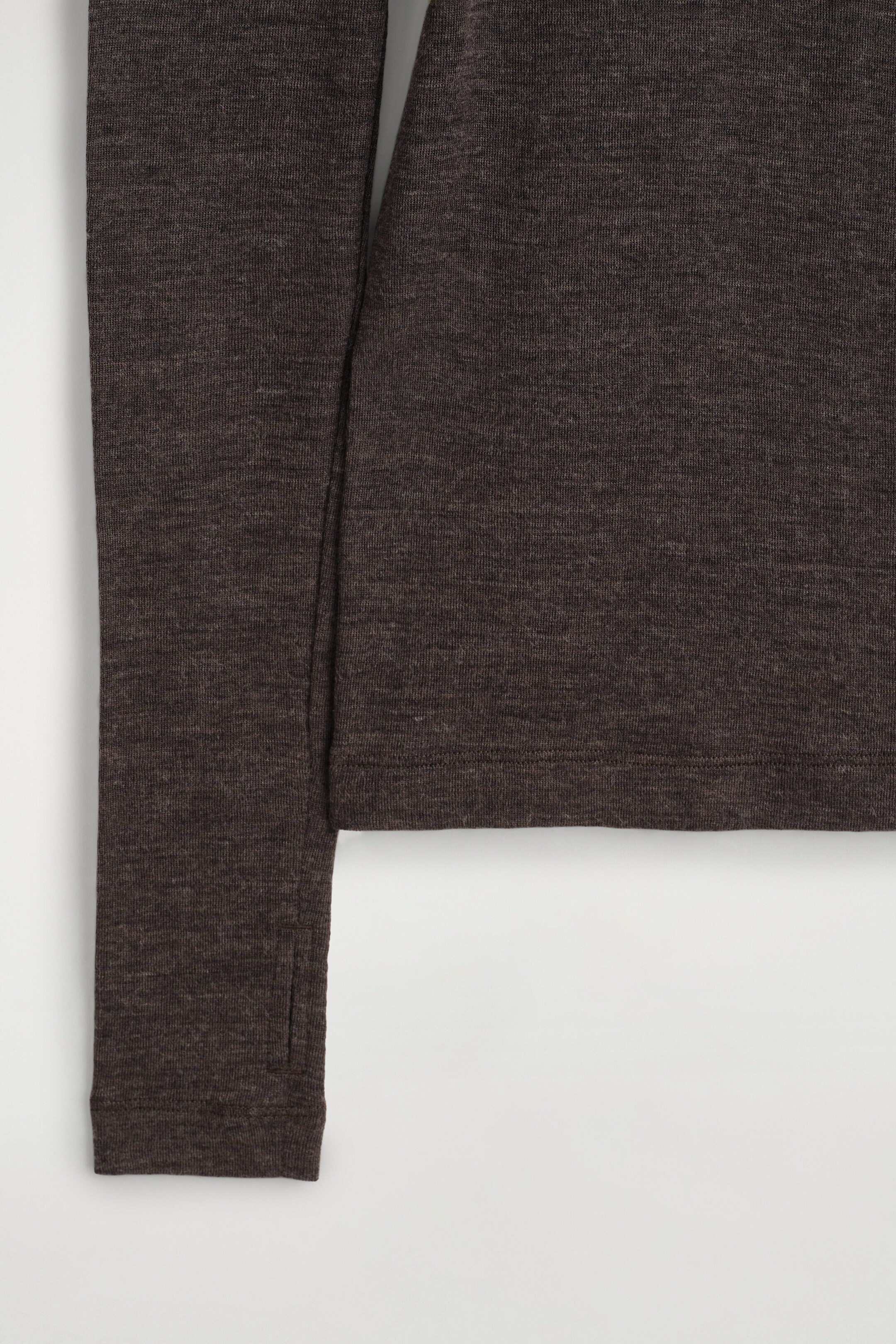 The merino wool high-neck top is displaying a dark brown heathered knit texture, featuring a straight stitched hem and a long sleeve with a built-in thumbhole detail near the cuff. The merino wool high-neck top is displaying a dark brown heathered knit texture, featuring a straight stitched hem and a long sleeve with a built-in thumbhole detail near the cuff.