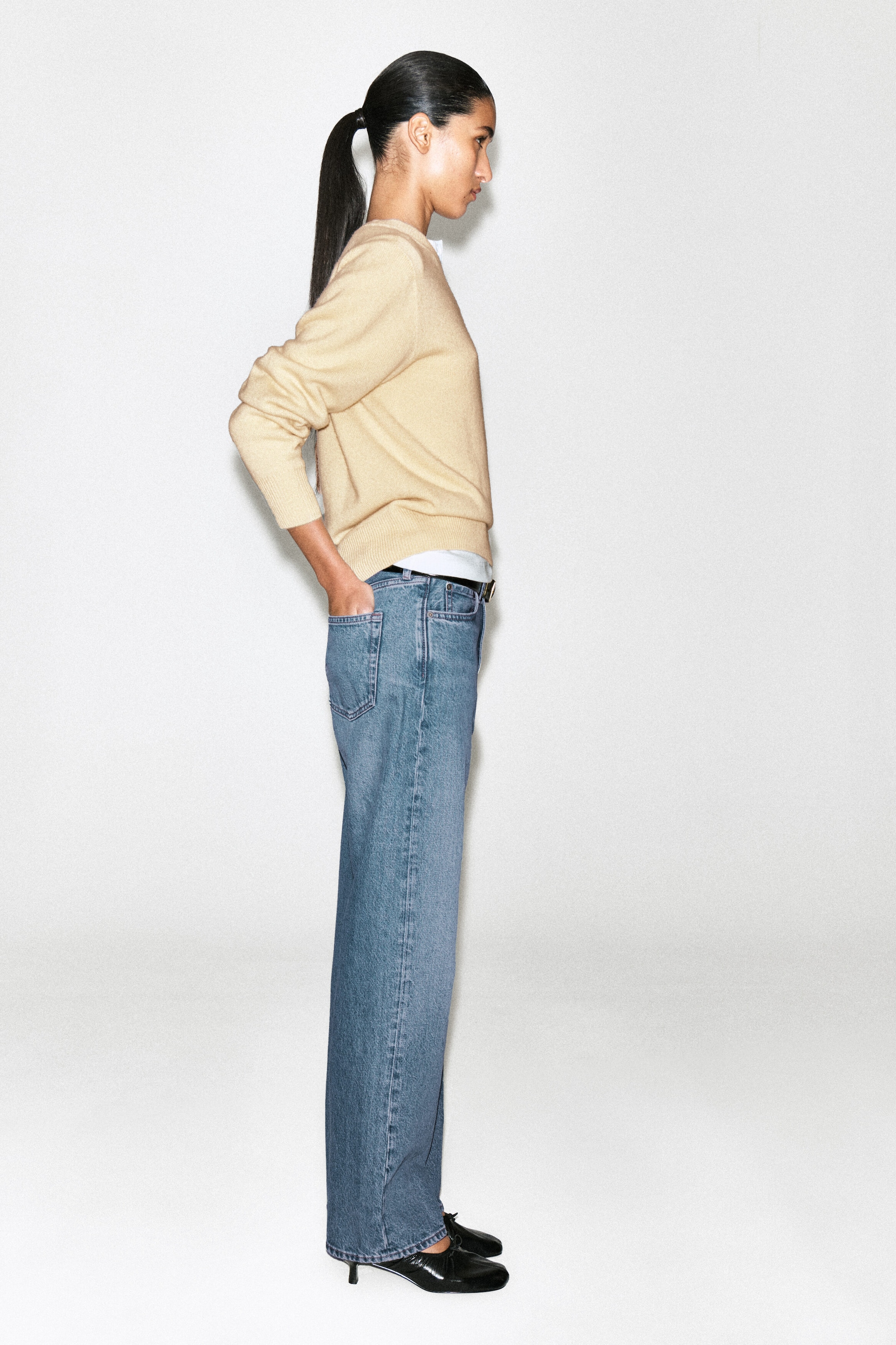 The Chord Straight-Leg Jeans present a classic straight-leg silhouette in medium-wash blue denim, shown from a side profile facing right to highlight the relaxed fit and back pocket structure. The jeans feature a mid-to-high rise waist styled with a thin black belt, a beige sweater, and black heeled shoes. The Chord Straight-Leg Jeans present a classic straight-leg silhouette in medium-wash blue denim, shown from a side profile facing right to highlight the relaxed fit and back pocket structure. The jeans feature a mid-to-high rise waist styled with a thin black belt, a beige sweater, and black heeled shoes.