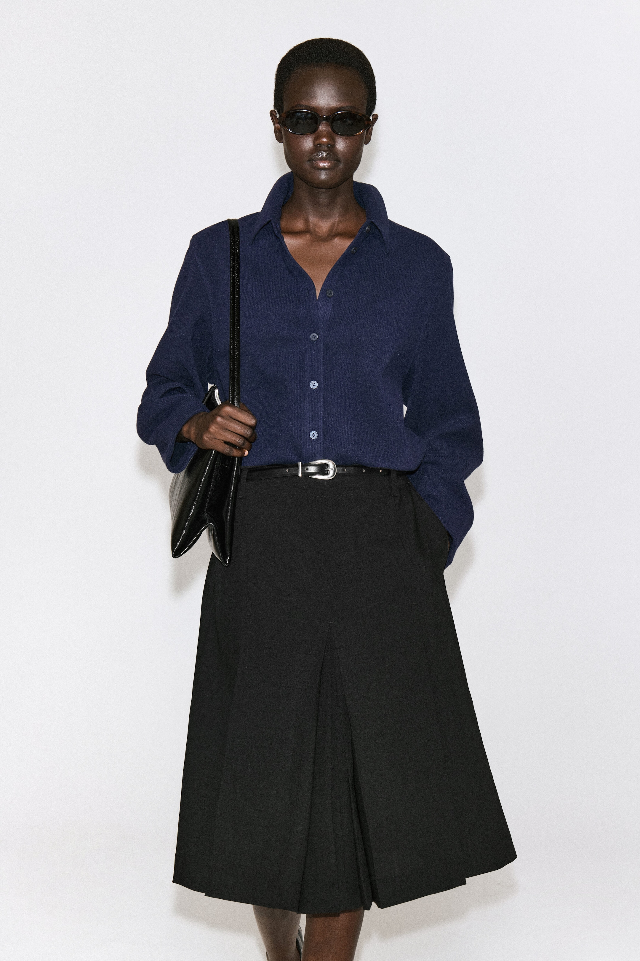 A navy blue corduroy jersey shirt is shown from the front, featuring a classic pointed collar, long sleeves, and a front button closure with color-matched buttons. The shirt is worn tucked into a belted black skirt, highlighting its relaxed fit and soft, textured fabric. A navy blue corduroy jersey shirt is shown from the front, featuring a classic pointed collar, long sleeves, and a front button closure with color-matched buttons. The shirt is worn tucked into a belted black skirt, highlighting its relaxed fit and soft, textured fabric.