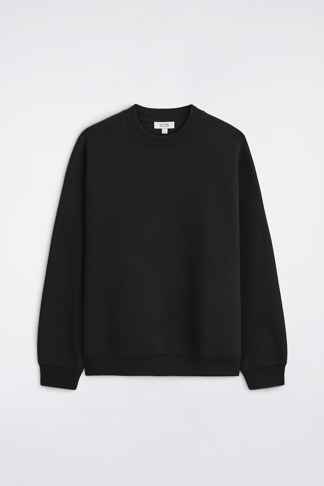 Bluza Relaxed Scuba jest pokazana z przodu i wyróżnia siÄ gÅadkÄ
, strukturalnÄ
czarnÄ
tkaninÄ
, obniżonÄ
liniÄ
ramion oraz dÅugimi rÄkawami. Bluza ma prÄ
żkowany okrÄ
gÅy dekolt, prÄ
żkowane mankiety i prÄ
żkowany dóÅ, które podkreÅlajÄ
jej swobodny fason. - 1