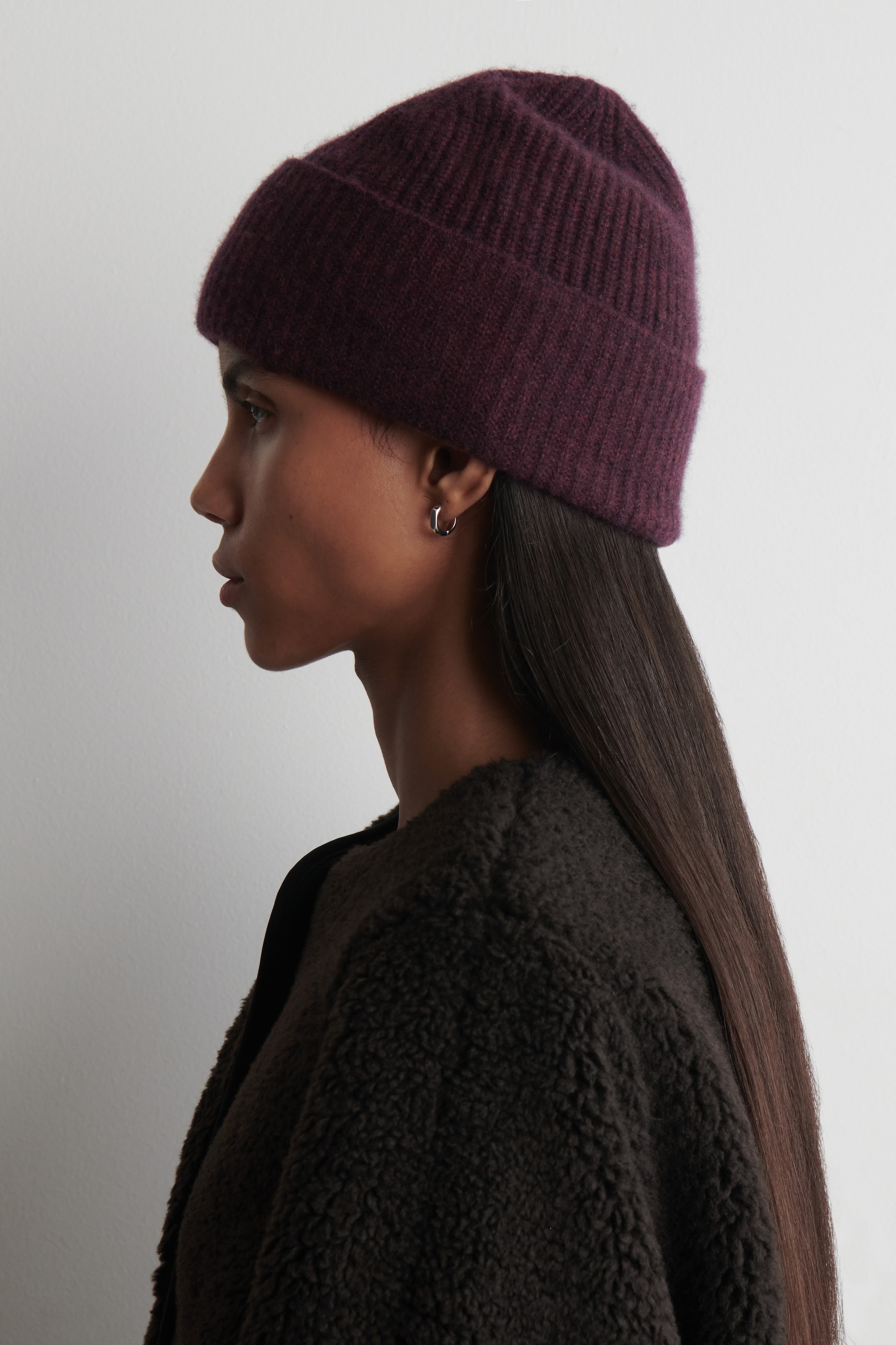 View larger image: A deep plum ribbed knit beanie is covering a person's head, shown from a side profile, with a visible folded cuff and a soft, slightly fuzzy texture.