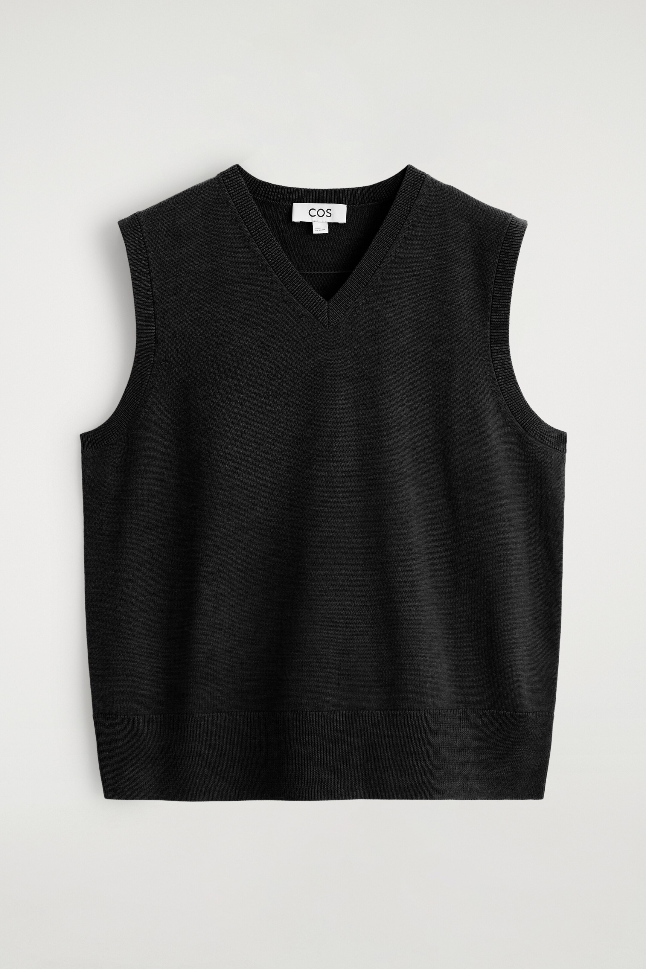 Visualizza immagine più grande: Un maglione nero senza maniche è mostrato dal davanti, con uno scollo a V e bordi a coste lungo lo scollo, i giromanica e l'orlo inferiore.