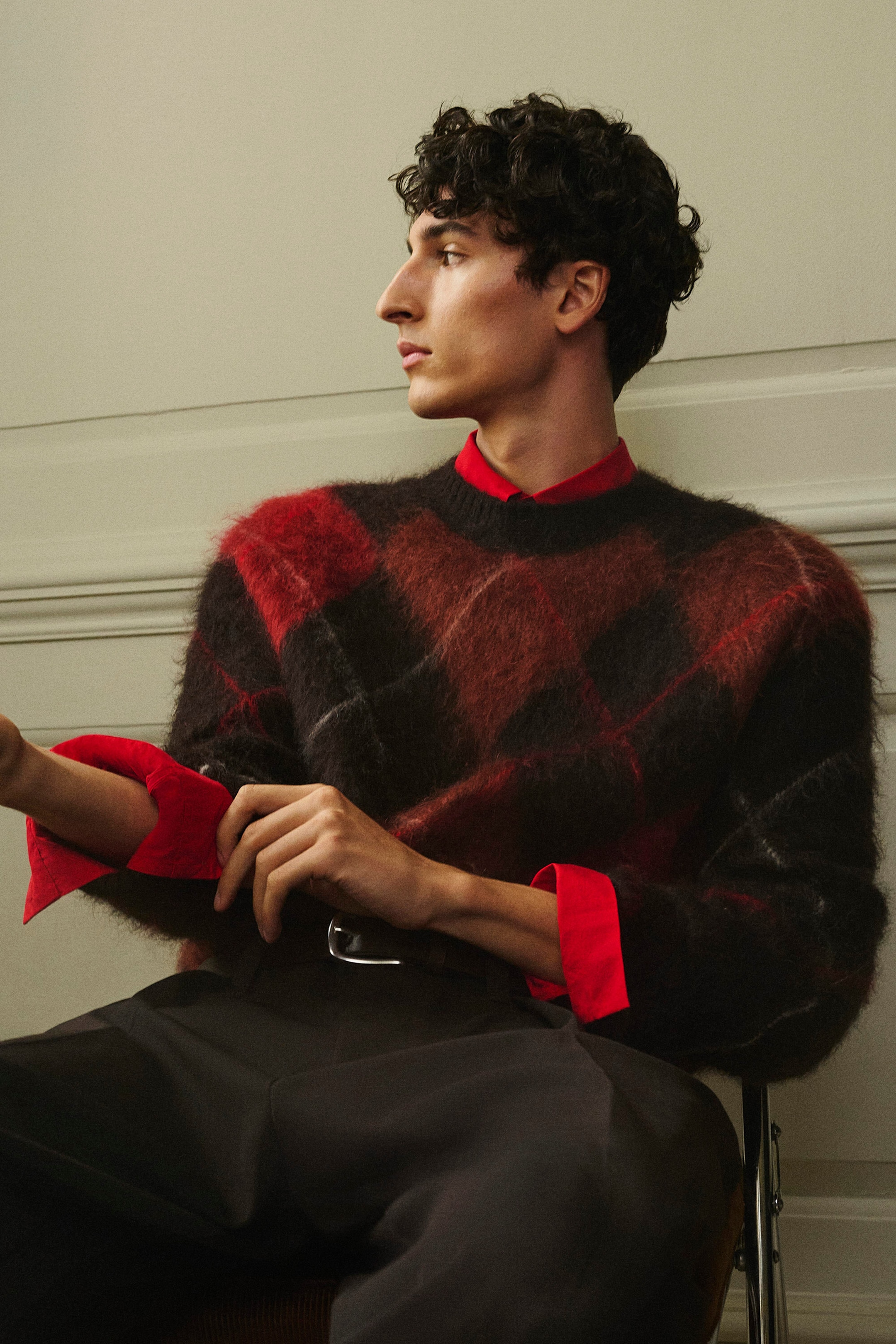 Le pull ras du cou en laine et mohair à motif argyle, doté d’une texture duveteuse et d’un motif losange rouge et noir, est présenté de face sur un mannequin assis. Ce vêtement en maille à coupe décontractée est superposé à une chemise à col rouge vif dont les poignets sont retroussés, et associé à un pantalon foncé. Le pull ras du cou en laine et mohair à motif argyle, doté d’une texture duveteuse et d’un motif losange rouge et noir, est présenté de face sur un mannequin assis. Ce vêtement en maille à coupe décontractée est superposé à une chemise à col rouge vif dont les poignets sont retroussés, et associé à un pantalon foncé.