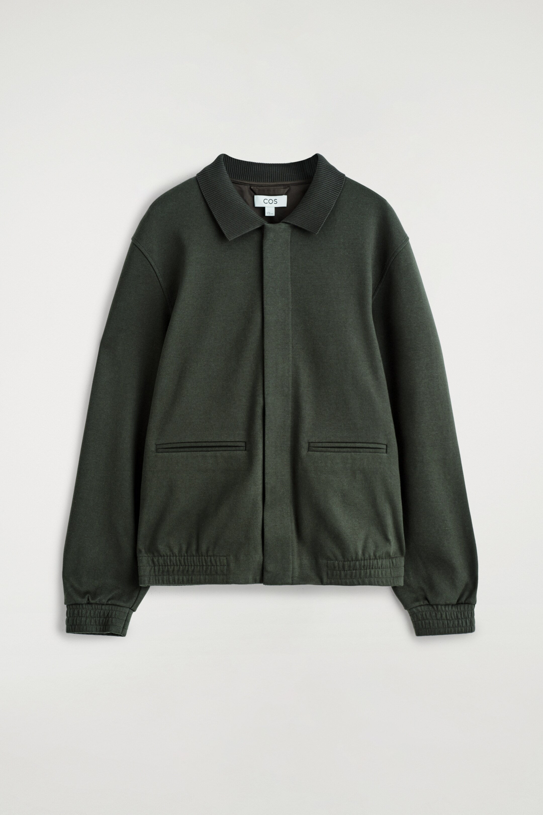 Agrandir l'image: Une veste Harrington en jersey vert foncé est présentée de FACE, avec un col côtelé, une fermeture à patte centrale, deux poches passepoilées et des poignets et un ourlet élastiqués.