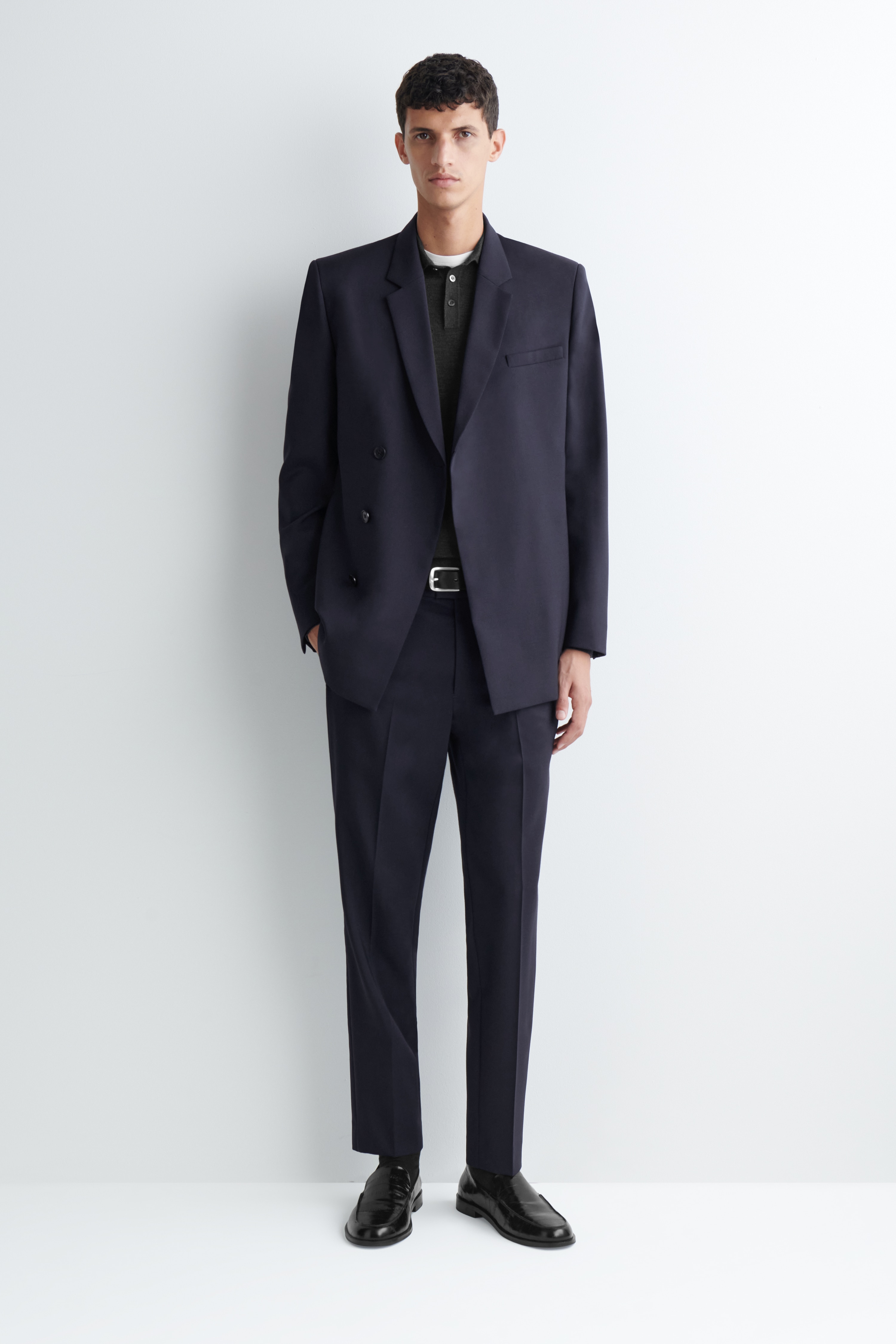 I pantaloni dritti slim fit in lana sono mostrati frontalmente, in un colore blu navy scuro, con vita strutturata con passanti per cintura e chiusura frontale nascosta. I pantaloni presentano pieghe nette stirate lungo il centro di თითო gamba e discrete tasche laterali a filo.