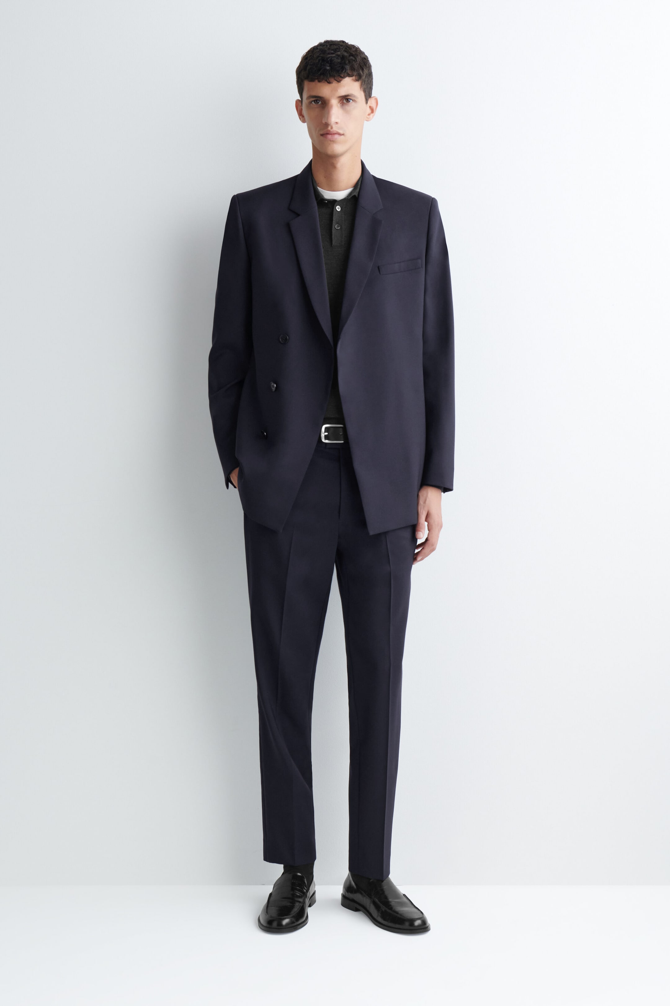 Un pantalon droit slim en laine bleu marine foncé est porté par le mannequin, avec des plis marqués et nets sur le devant. Le pantalon est associé à une ceinture en cuir noire, à un blazer croisé assorti et à des mocassins en cuir noirs. Un pantalon droit slim en laine bleu marine foncé est porté par le mannequin, avec des plis marqués et nets sur le devant. Le pantalon est associé à une ceinture en cuir noire, à un blazer croisé assorti et à des mocassins en cuir noirs.
