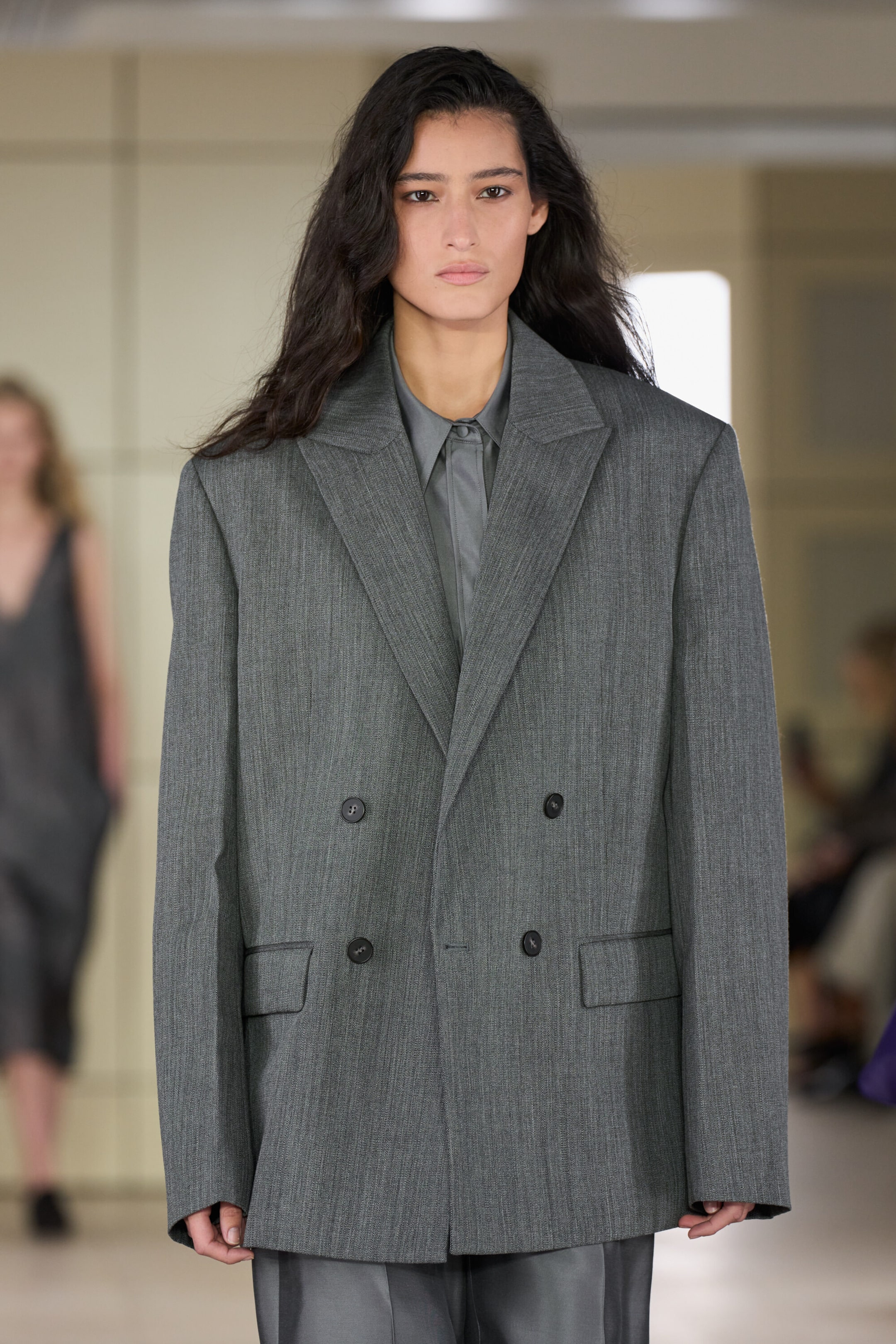 A tailored silk shirt in a muted gray tone is shown from the front, featuring a classic pointed collar and a smooth, lustrous fabric. The shirt is layered beneath a structured, oversized gray double-breasted blazer with peak lapels. A tailored silk shirt in a muted gray tone is shown from the front, featuring a classic pointed collar and a smooth, lustrous fabric. The shirt is layered beneath a structured, oversized gray double-breasted blazer with peak lapels.