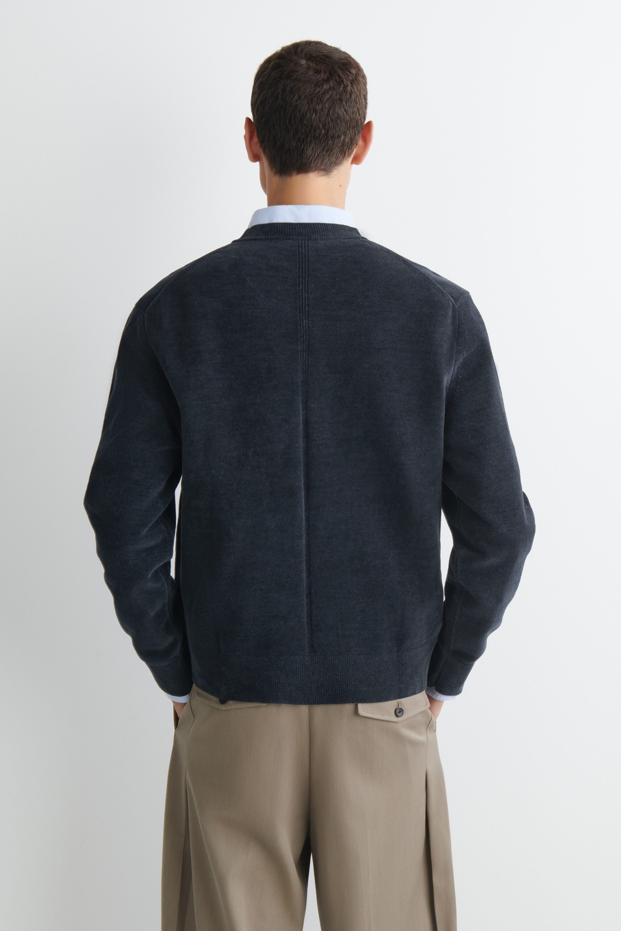 The cotton chenille crew neck sweater, shown from the back, features a textured dark gray fabric and a prominent vertical seam running down the center of the back. It has ribbed detailing at the collar, cuffs, and hem, and is layered over a light blue collared shirt. The cotton chenille crew neck sweater, shown from the back, features a textured dark gray fabric and a prominent vertical seam running down the center of the back. It has ribbed detailing at the collar, cuffs, and hem, and is layered over a light blue collared shirt.