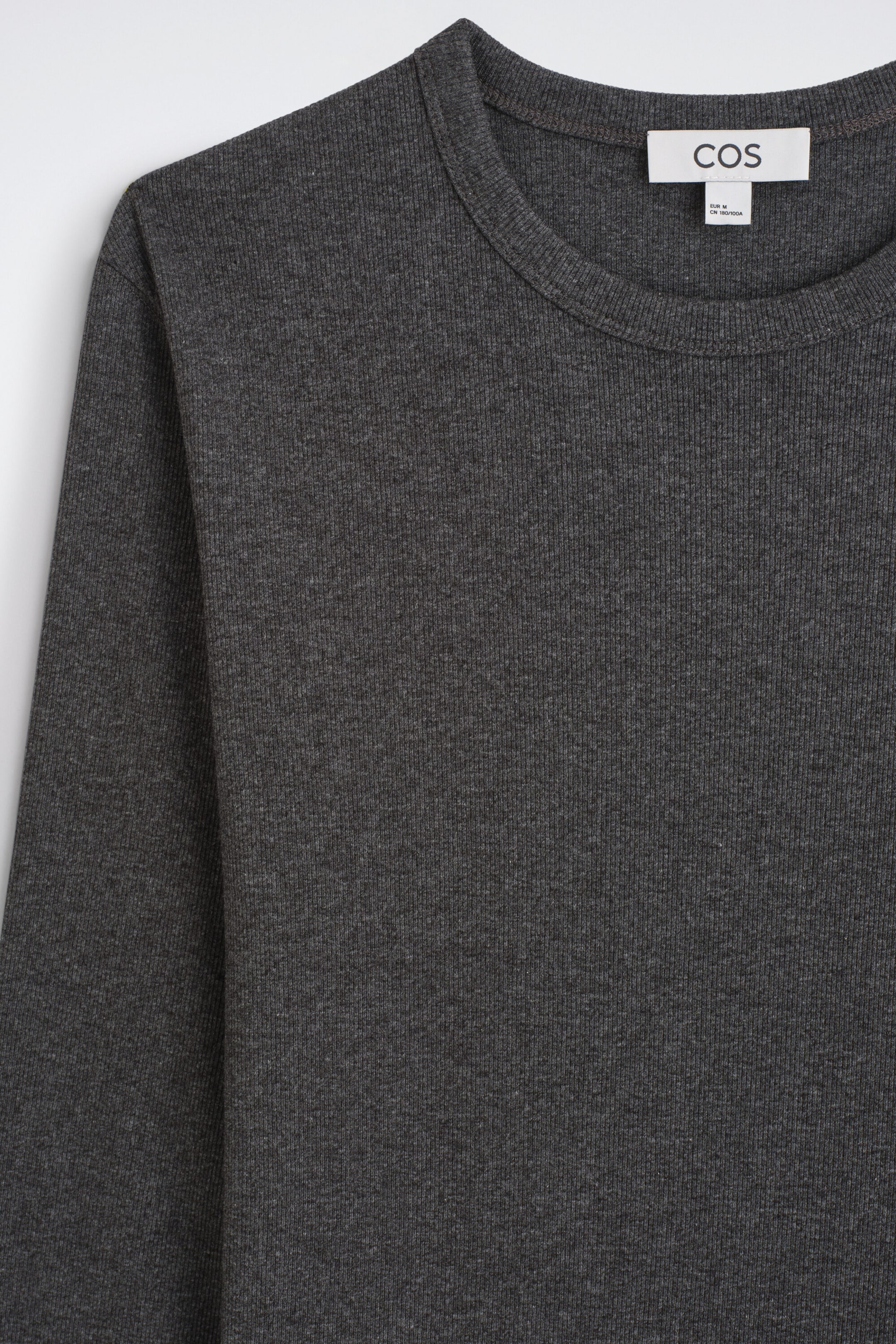 A dark gray ribbed knit crewneck top is shown in a close-up front view, featuring a fine vertical ribbed texture, a classic crew neckline, and a white brand label inside the collar. A dark gray ribbed knit crewneck top is shown in a close-up front view, featuring a fine vertical ribbed texture, a classic crew neckline, and a white brand label inside the collar.