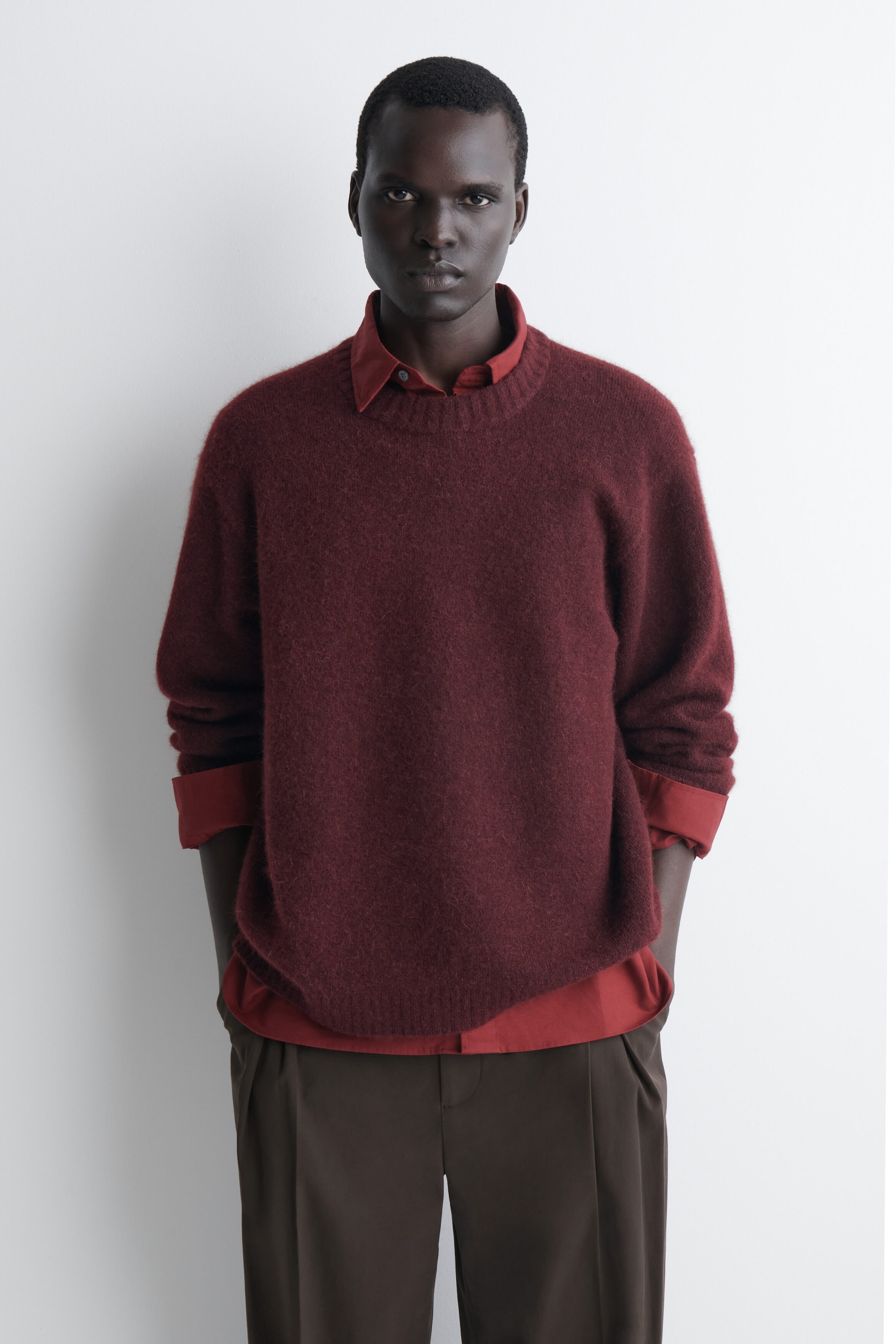 The oversized alpaca-blend crew-neck sweater in a deep burgundy hue is shown from the front, highlighting its fuzzy knit texture, relaxed fit, and ribbed trims. It is being layered over a coordinating red collared shirt, with the collar and hem visibly peeking out. The oversized alpaca-blend crew-neck sweater in a deep burgundy hue is shown from the front, highlighting its fuzzy knit texture, relaxed fit, and ribbed trims. It is being layered over a coordinating red collared shirt, with the collar and hem visibly peeking out.