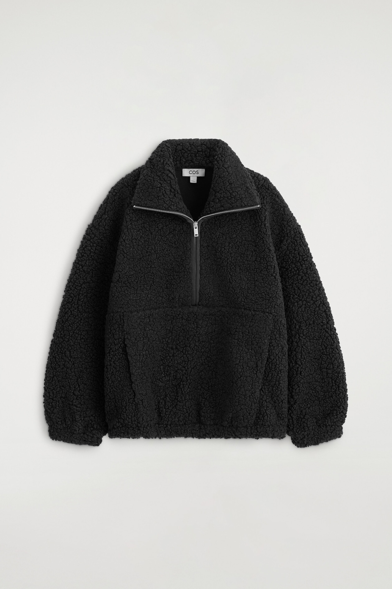 La vue de face montre le chandail teddy noir à col cheminée zippé, avec un tissu polaire texturé et un col montant muni d'une fermeture demi-zip argentée. Le design comprend des manches longues avec poignets élastiqués et une grande poche kangourou à l'avant.