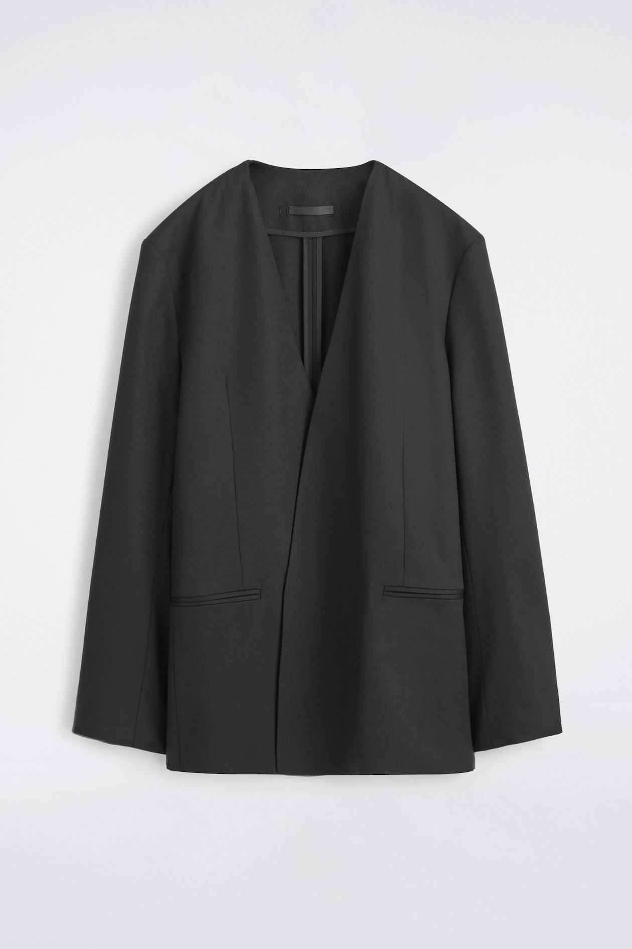 A black blazer features a collarless, open-front design with wide, flat lapels forming a deep V-neckline. Long sleeves and two horizontal welt pockets are visible on the front.