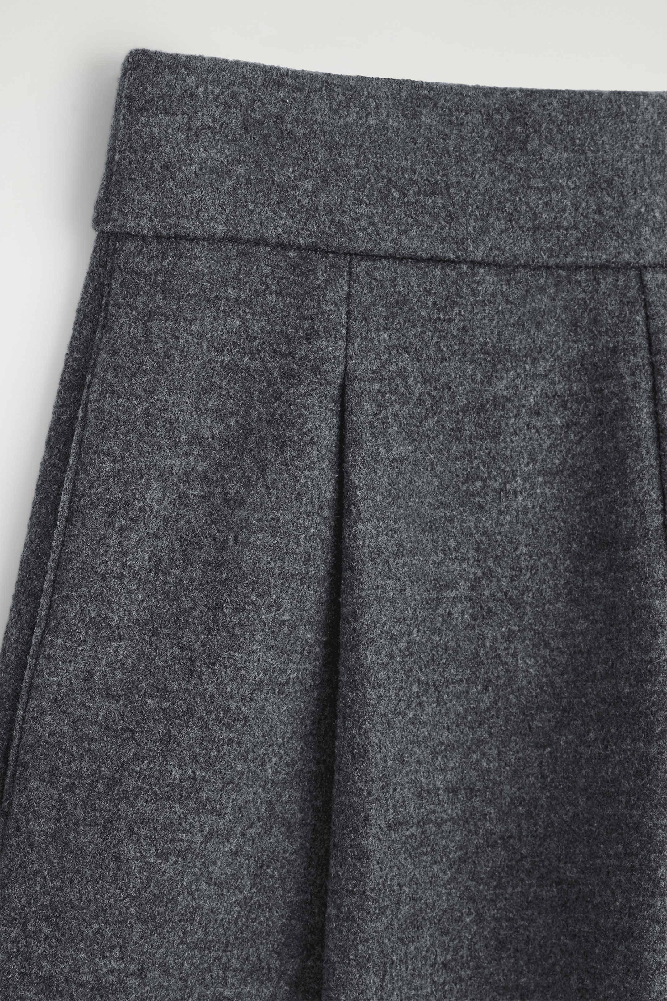 View larger image: Dark gray trousers are being presented from the FRONT, featuring a wide, flat waistband and two vertical pleats. The fabric is displaying a dense, felted texture.