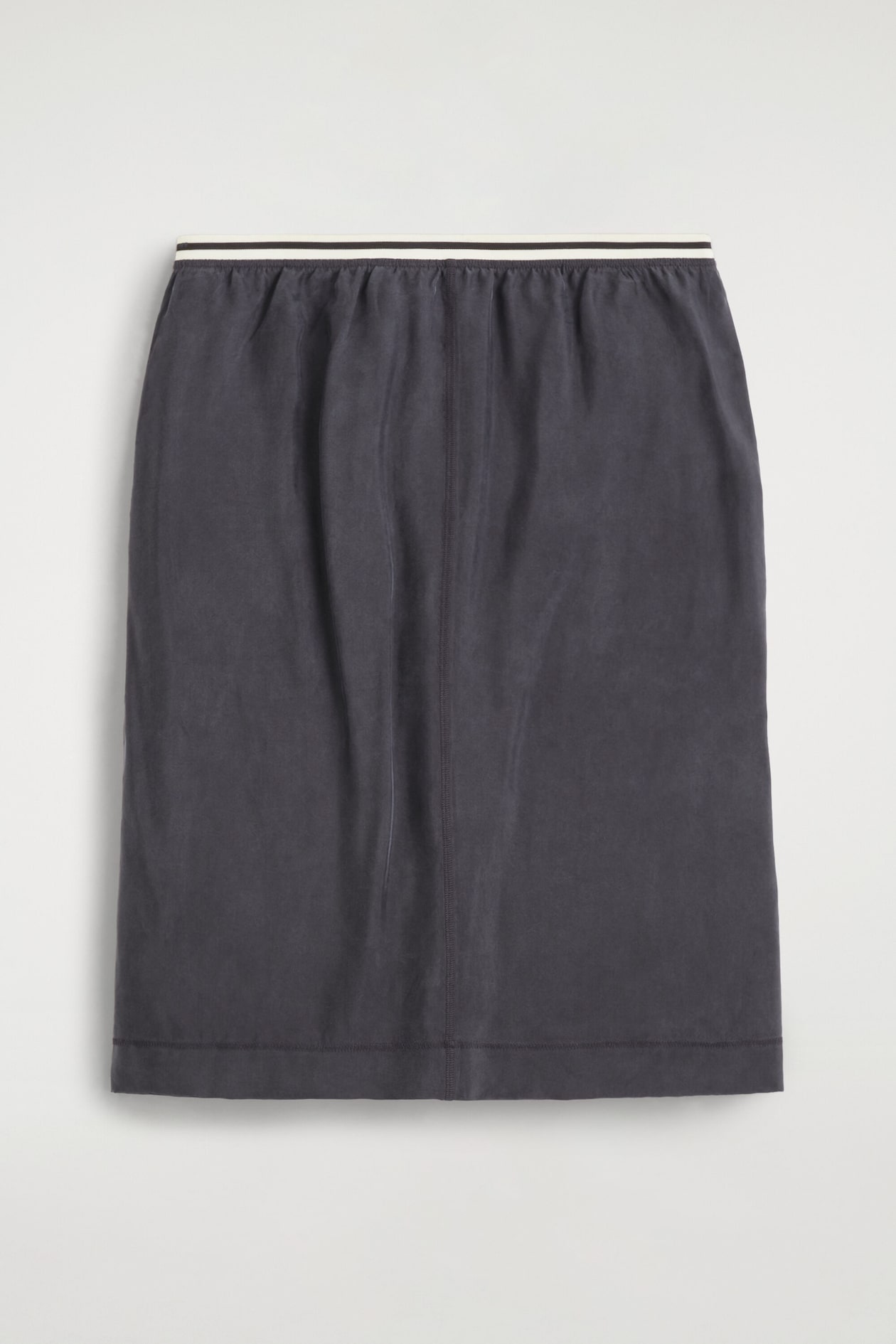 A dark gray pencil skirt is shown from the front, featuring an elastic waistband with a white stripe flanked by thin black stripes, and gathered fabric below it. A vertical center front seam runs down to a straight hem.