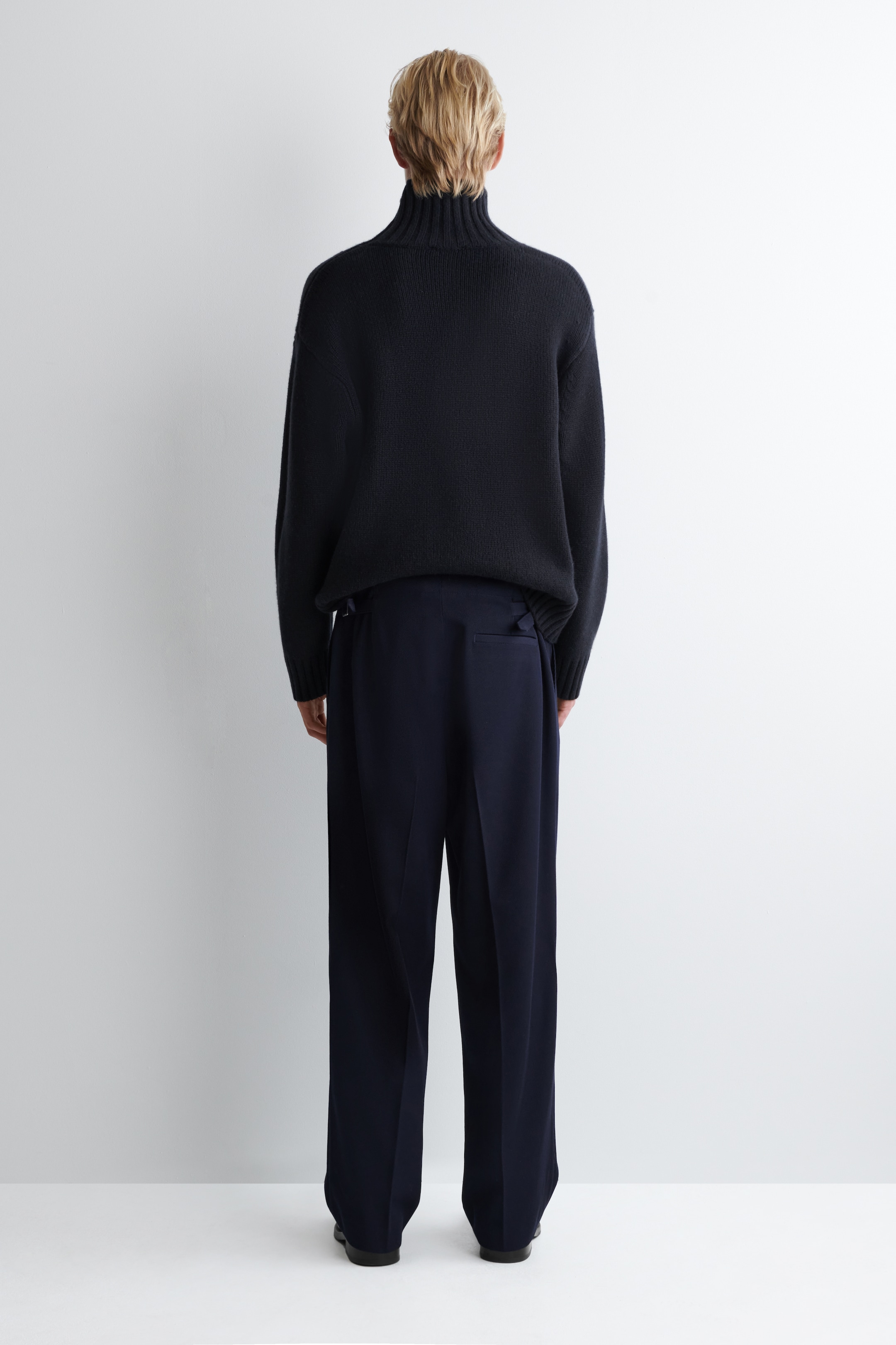 Agrandir l'image: Une tenue bleu marine foncé est présentée de dos, composée d'un pull à col roulé à coupe décontractée et d'un pantalon à jambes larges. Le pull présente un tricot texturé, tandis que le pantalon affiche des ajusteurs de taille arrière visibles.