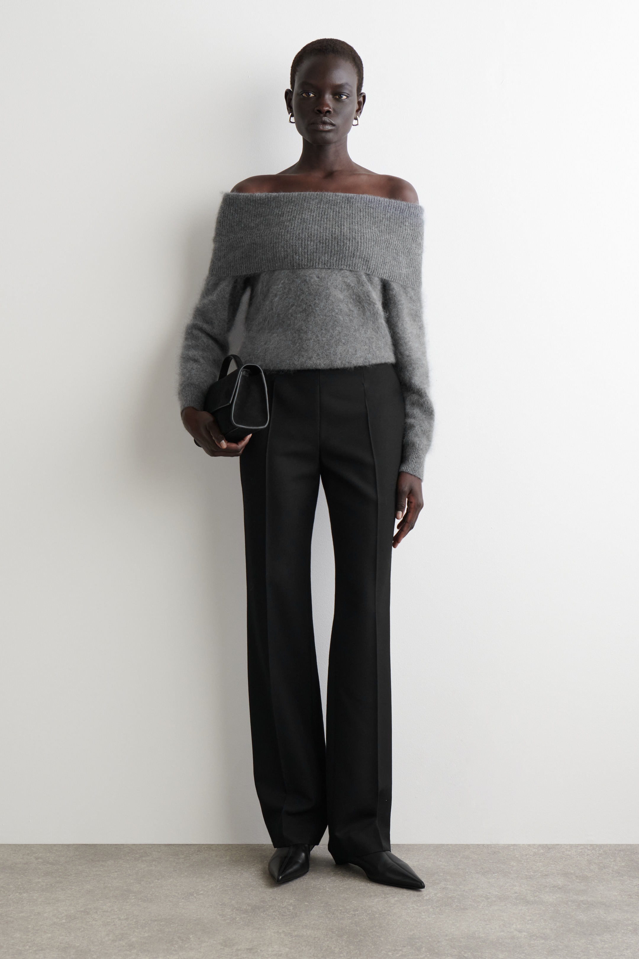 Ver imagen más grande: Un suéter gris sin hombros se presenta desde una vista frontal, con un escote ancho de canalé y una textura peluda en sus mangas largas. Se combina con pantalones negros de pierna ancha, zapatos negros de punta y un pequeño bolso negro estructurado.