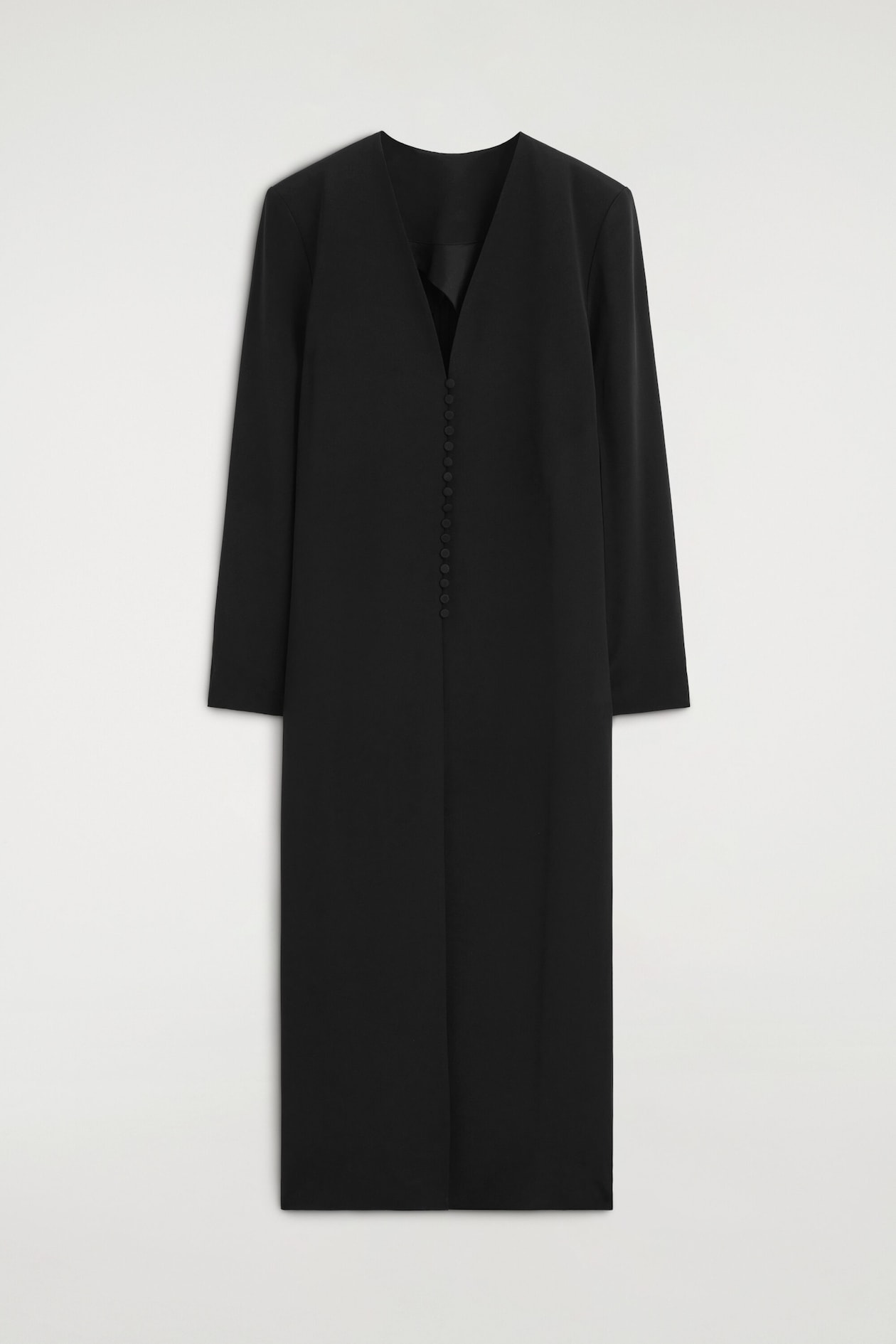 Ein schwarzes, knielanges Kleid zeigt von vorne eine gerade, strukturierte Silhouette. Es verfügt über einen kragenlosen, tiefen V-Ausschnitt, lange Ärmel und eine vertikale Reihe kleiner, mit Stoff bezogener Knöpfe, die mittig vorne verläuft.