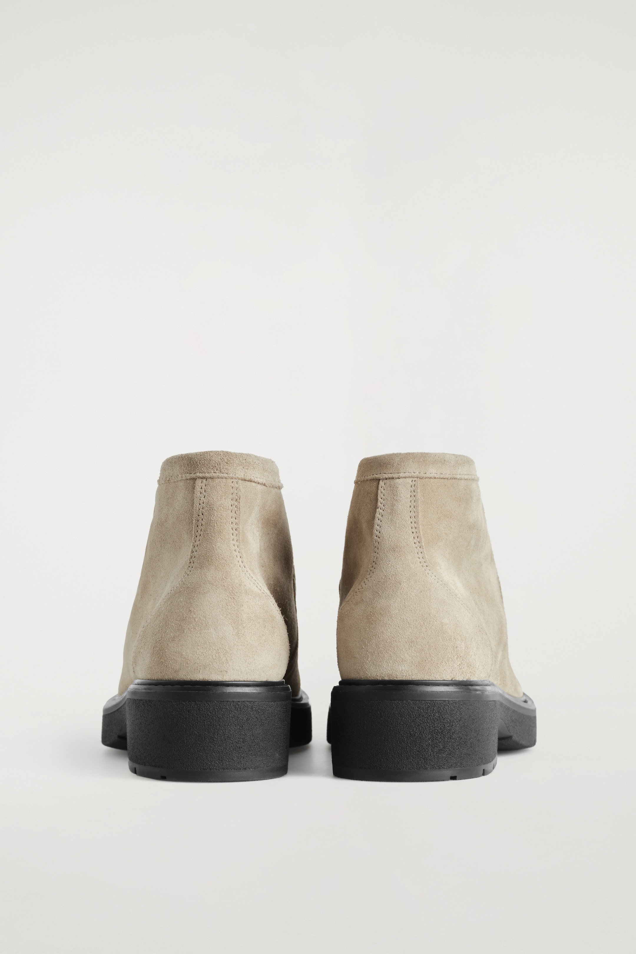 Agrandir l'image: Une paire de bottines en daim beige clair est orientée vers l'arrière, avec des surpiqûres ton sur ton le long de l'arrière de leurs tiges et des semelles épaisses contrastantes noires.