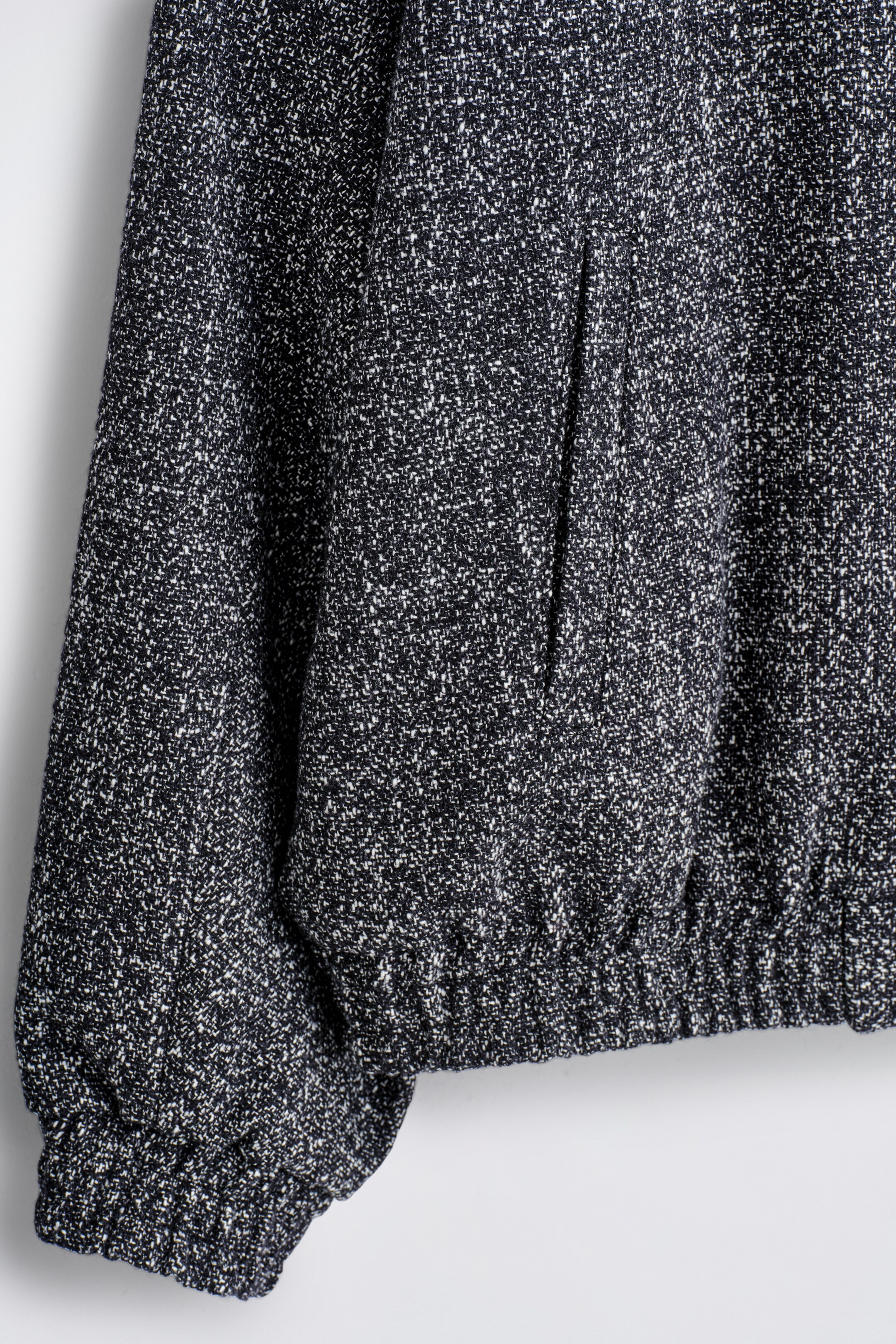 Grösseres Bild ansehen: Diese Track-Jacke präsentiert einen dunklen, gesprenkelten Tweed-Stoff mit einer sichtbaren vertikalen Leistentasche auf der Vorderseite. Sie verfügt auch über einen elastischen Saum und elastische Bündchen.