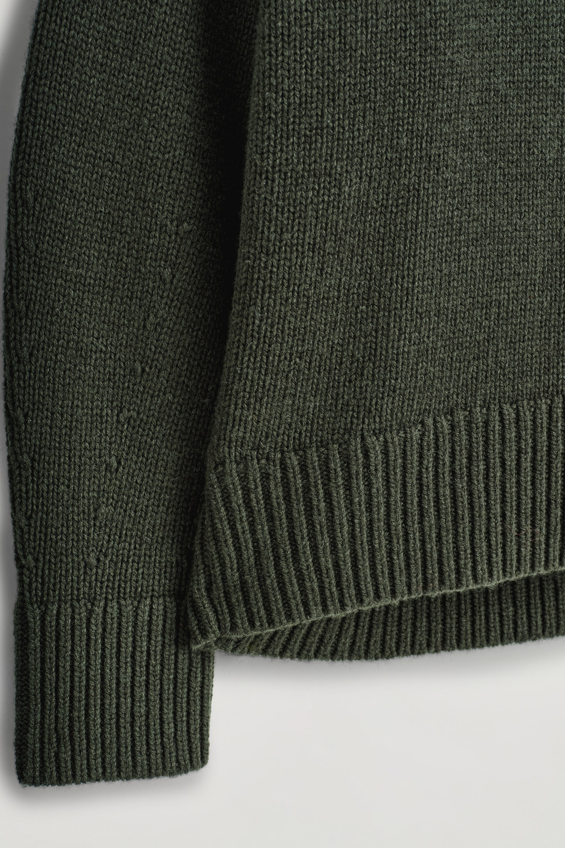 Größeres Bild anzeigen: Ein dunkelgrüner gestrickter Pullover verfügt über ein geripptes Bündchen und einen gerippten Saum. Der Hauptteil des Kleidungsstücks zeigt eine glatte Strickstruktur.