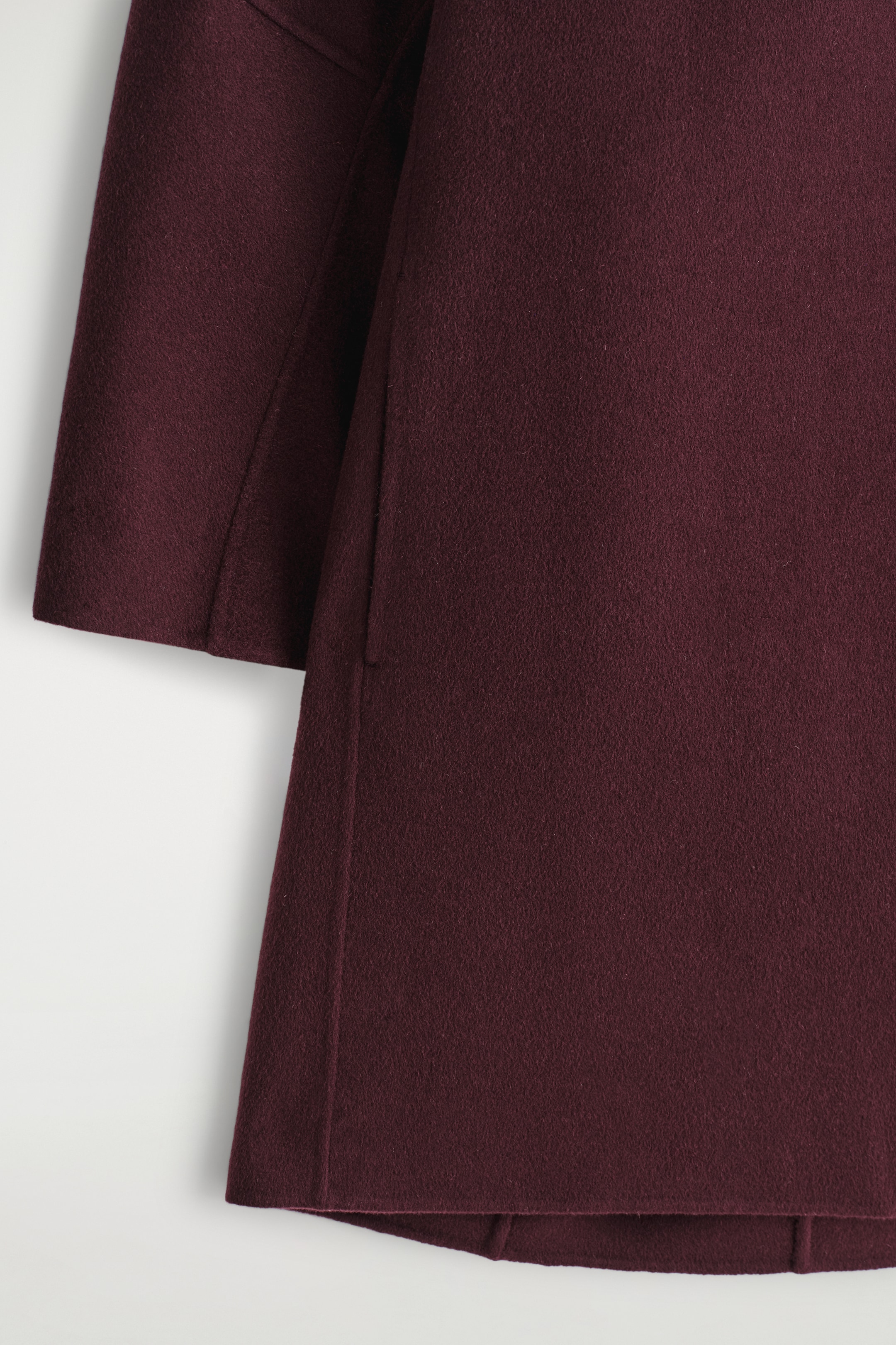 Agrandir l'image: La robe mini en laine double-face bordeaux profond présente un tissu doux et texturé. Une large manche à coupe droite est visible sur le côté gauche, et une poche latérale dans la couture est subtilement intégrée dans le panneau avant, qui se termine par un ourlet droit et net.