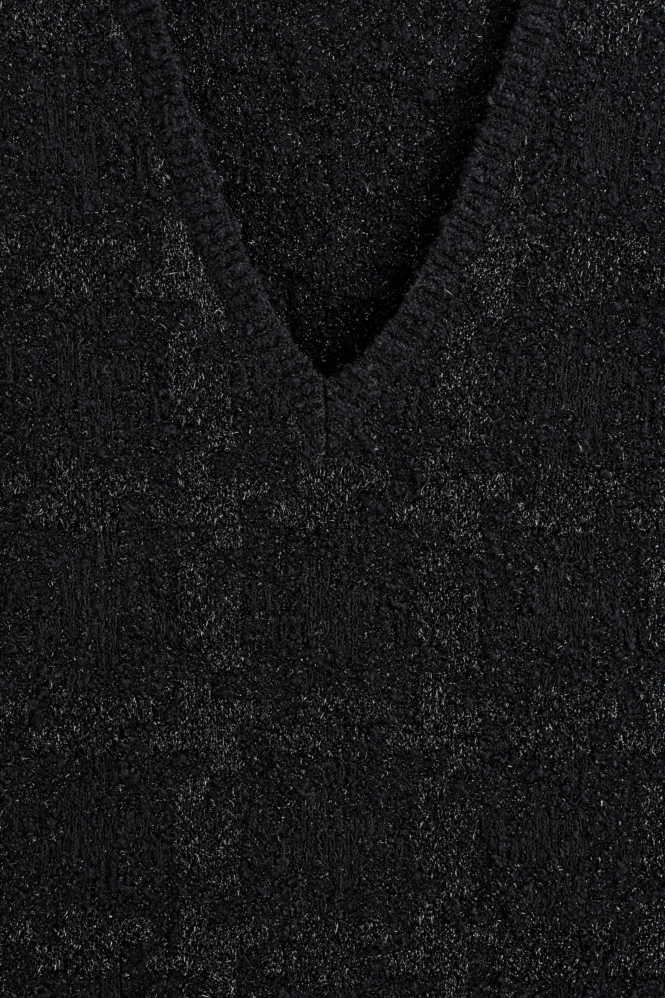 Agrandir l'image: Un gilet noir à col en V, fabriqué à partir d'un tissu texturé en maille bouclé, présente des fils argentés captant la lumière et un motif discret à carreaux fenêtre.