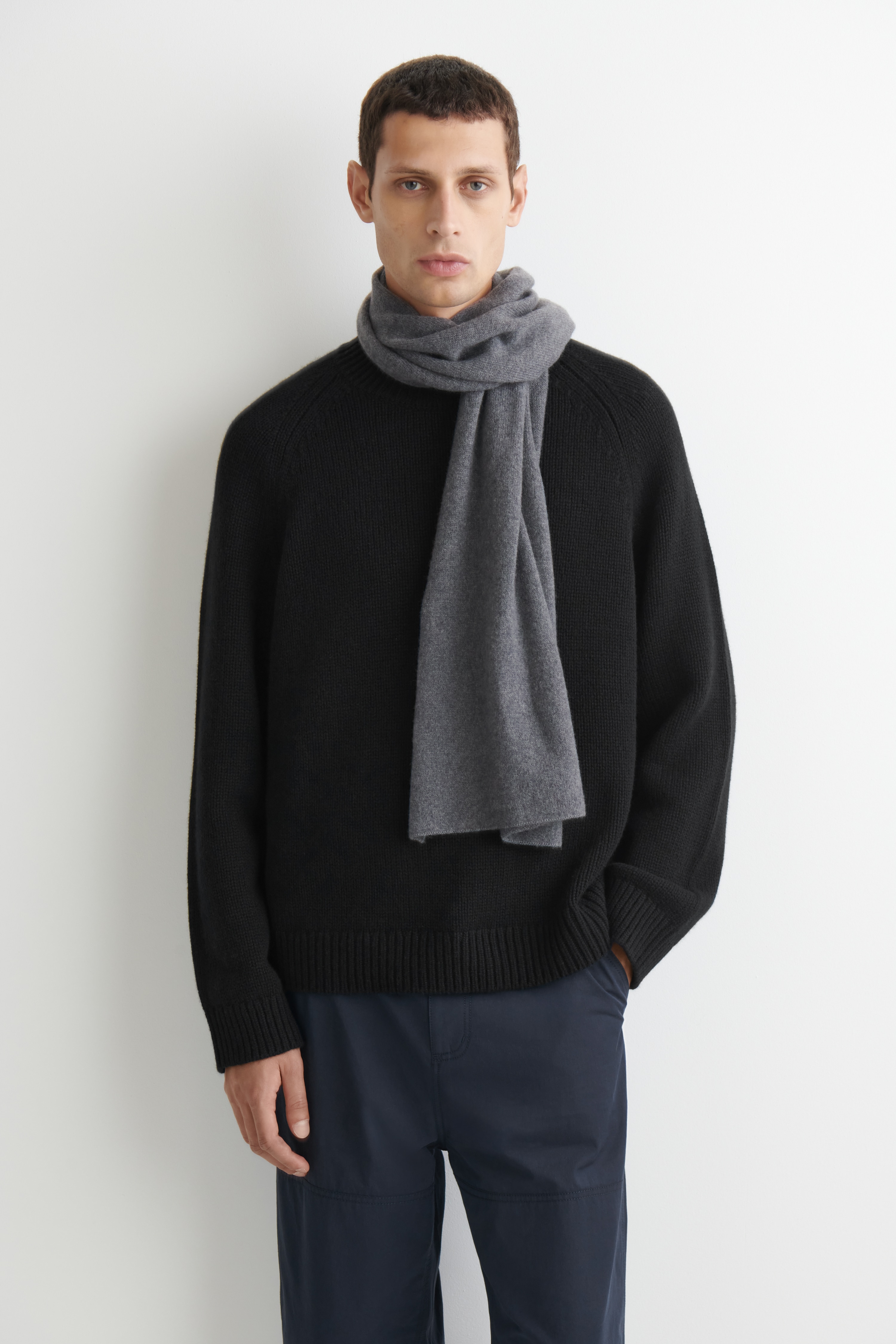 Una sciarpa in cashmere Ã¨ disposta piatta e piegata a quadrato, mettendo in risalto il suo colore grigio scuro mÃ©lange e la sua morbida texture a maglia fine. Unâetichetta bianca del marchio Ã¨ posizionata nellâangolo inferiore sinistro, con il logo âCOSâ e la scritta â100% CASHMEREâ.
