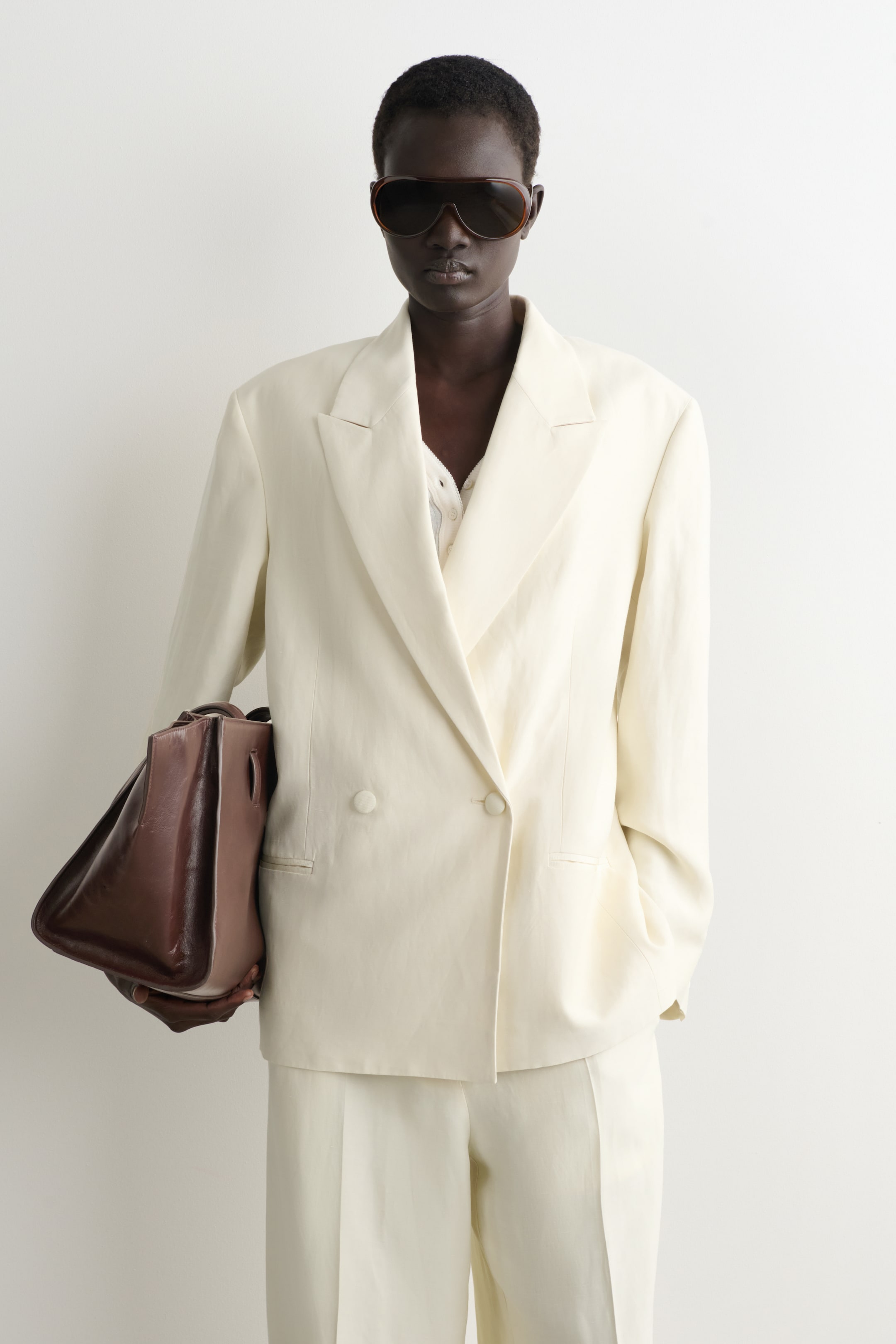 Agrandir l'image: Un blazer crème à double boutonnage avec des revers en pointe présente une coupe décontractée, superposé sur un haut blanc. Un pantalon crème assorti, de style jambes larges, complète cet ensemble de costume.