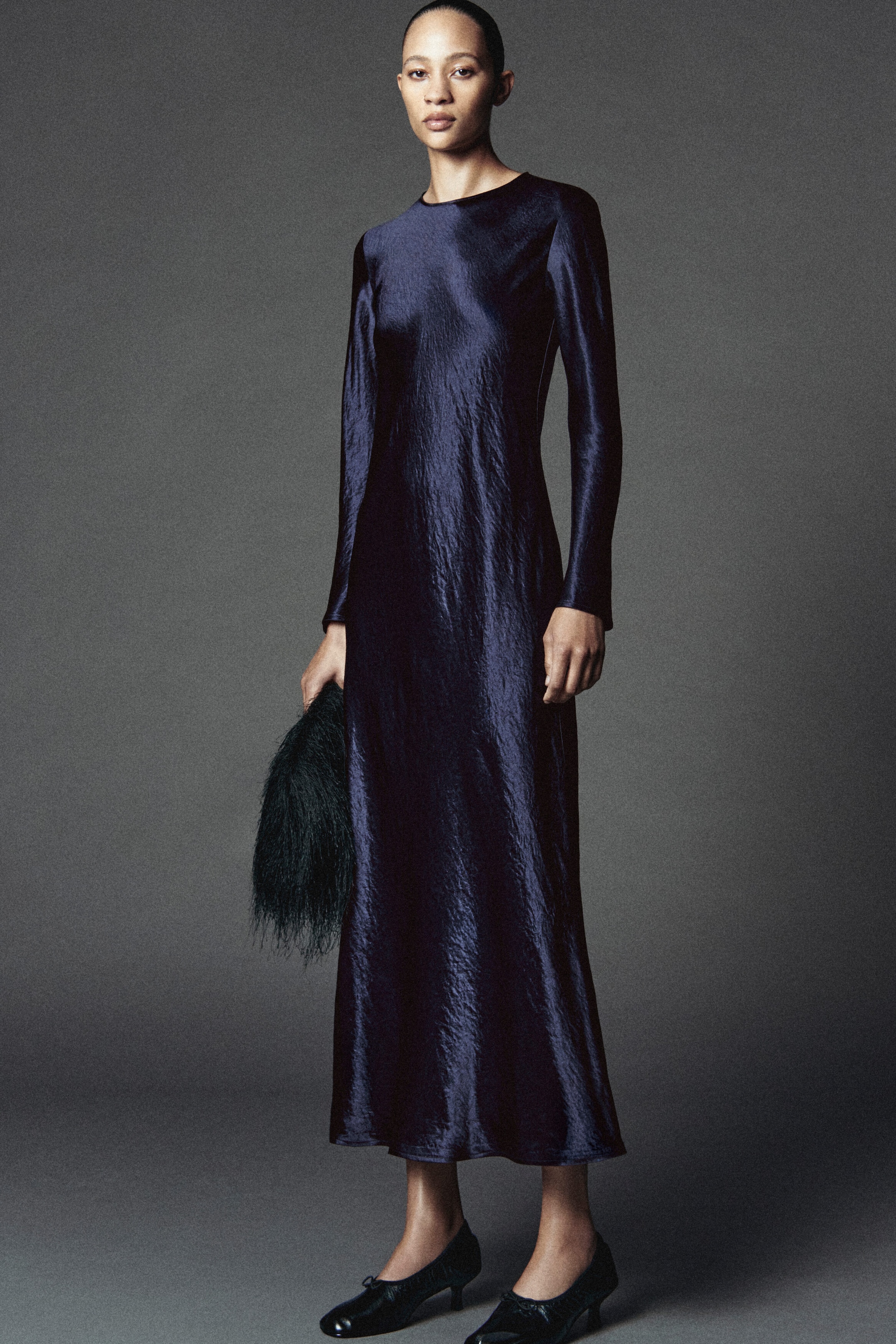 This satin long-sleeved maxi dress in deep navy blue is shown front-facing, featuring a textured, crinkled fabric with a subtle sheen. The dress falls in a fluid, straight silhouette to the ankles and is designed with a high round neckline and long fitted sleeves. This satin long-sleeved maxi dress in deep navy blue is shown front-facing, featuring a textured, crinkled fabric with a subtle sheen. The dress falls in a fluid, straight silhouette to the ankles and is designed with a high round neckline and long fitted sleeves.