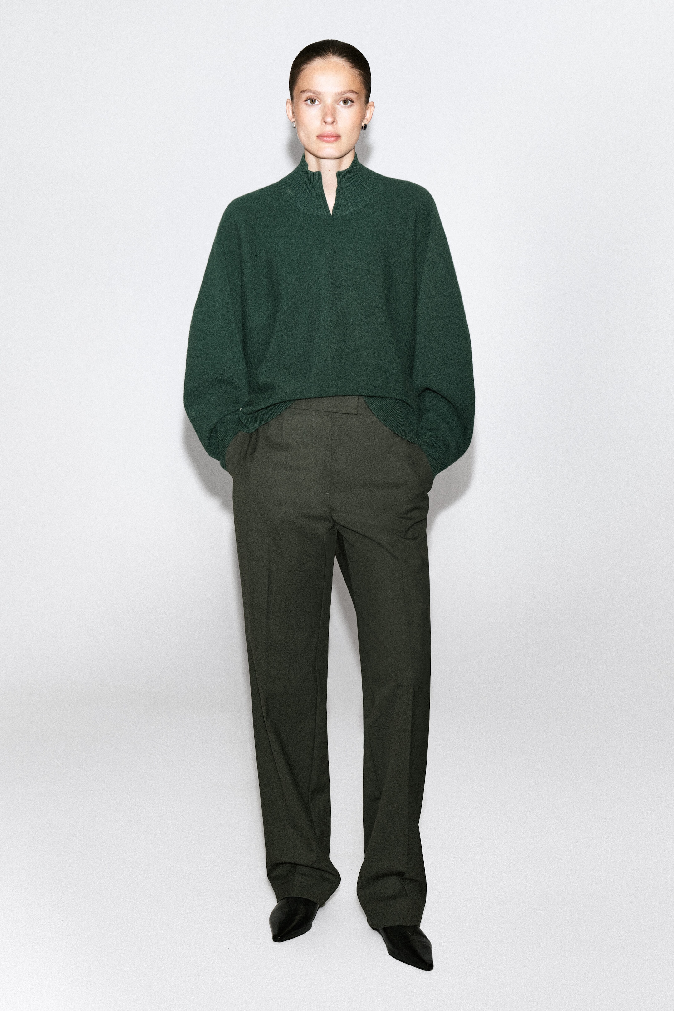 Le mannequin porte un pull en laine mérinos bouillie vert foncé, doté d’un col cheminée côtelé et d’un détail en V à l’avant. Ce pull à coupe décontractée est stylé rentré dans un pantalon foncé sur mesure. Le mannequin porte un pull en laine mérinos bouillie vert foncé, doté d’un col cheminée côtelé et d’un détail en V à l’avant. Ce pull à coupe décontractée est stylé rentré dans un pantalon foncé sur mesure.