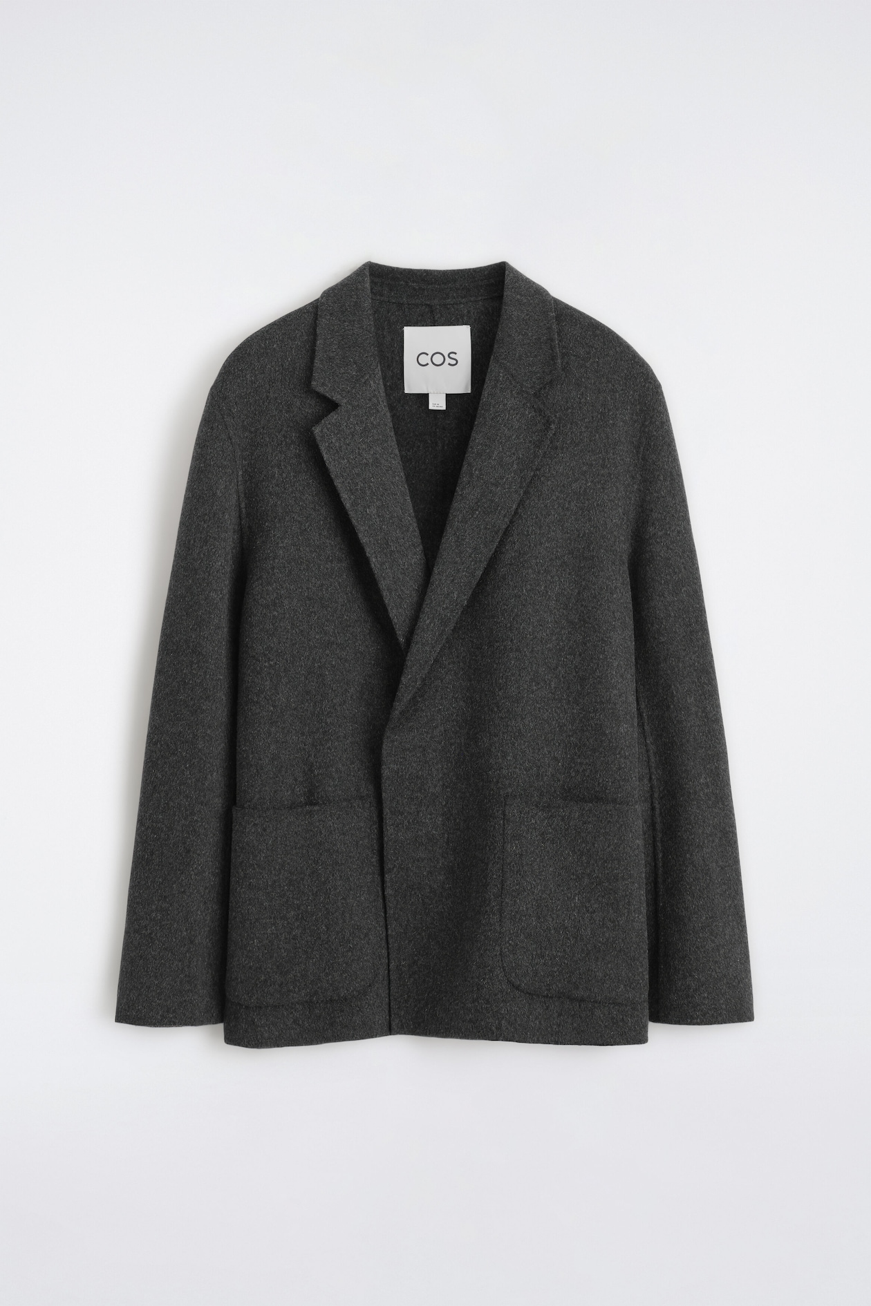 A dark grey, unstructured wool-blend blazer is shown in a front view, featuring notch lapels, a clean overlapping front, and two large front patch pockets. The relaxed-fit jacket is hanging flat, highlighting its soft textured fabric and clean-cut design.