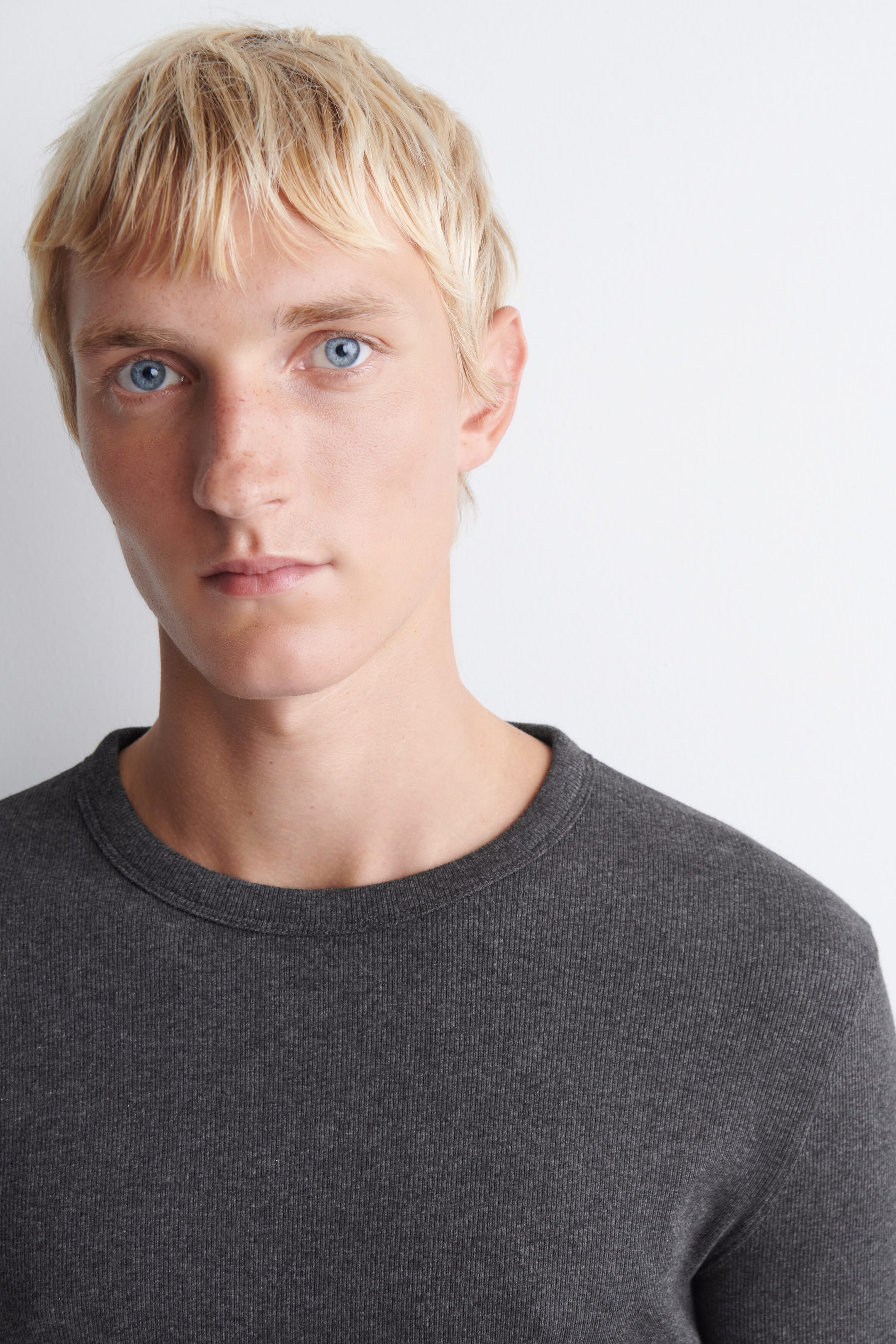 A dark gray crewneck top is shown from the front, featuring a fine ribbed knit texture and a banded collar. The garment fits snugly around the neckline and shoulders, highlighting its soft, textured construction.
