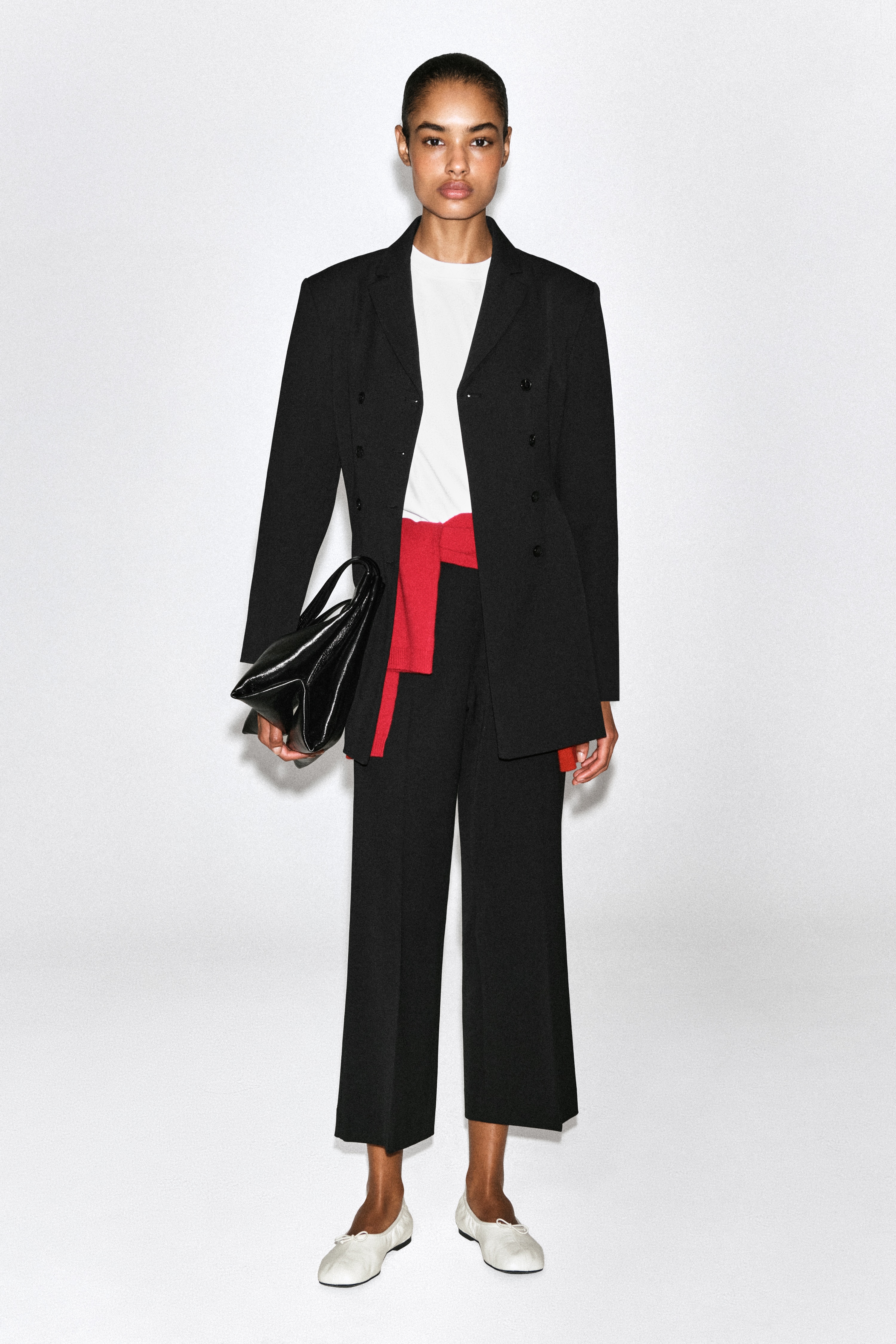 These black cropped flared trousers are shown from the front, featuring a clean, high-waisted design. Sharp pressed creases run down the centre of each leg, which widens towards the hem to create a structured, flared silhouette.