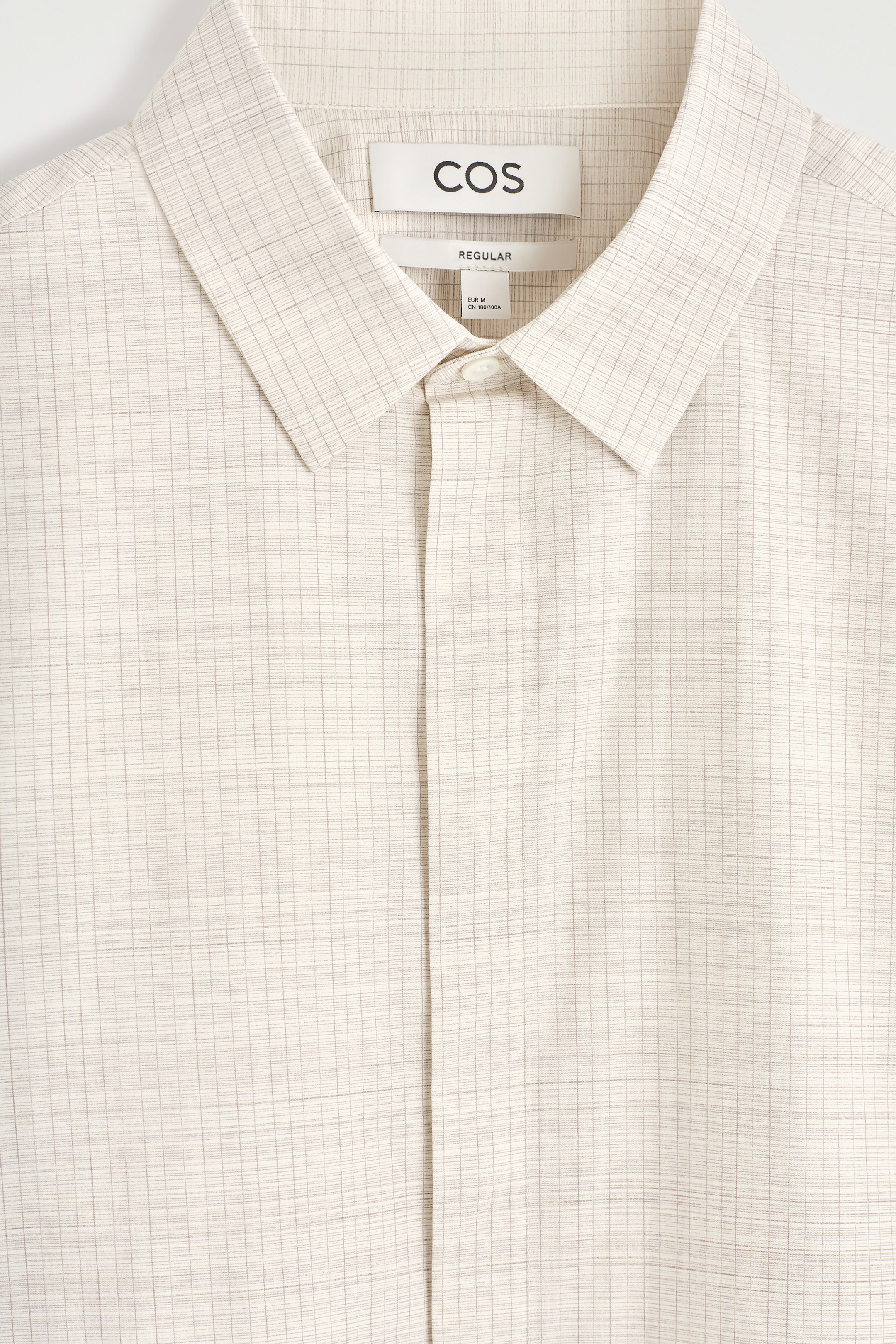 Visualizza immagine più grande: La parte anteriore di una camicia beige chiaro presenta un motivo a sottili righe sottili. È caratterizzata da un colletto appuntito e da un bottone in madreperla visibile nella parte superiore della sua abbottonatura.