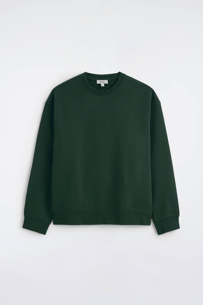 Ein Sweatshirt aus gewaschener Baumwolle in DunkelgrÃ¼n ist von vorne zu sehen und zeichnet sich durch eine lockere Passform mit Ã¼berschnittenen Schultern und langen Ãrmeln aus. Es prÃ¤sentiert einen gerippten Rundhalsausschnitt, gerippte BÃ¼ndchen und einen gerippten Saum. - 1