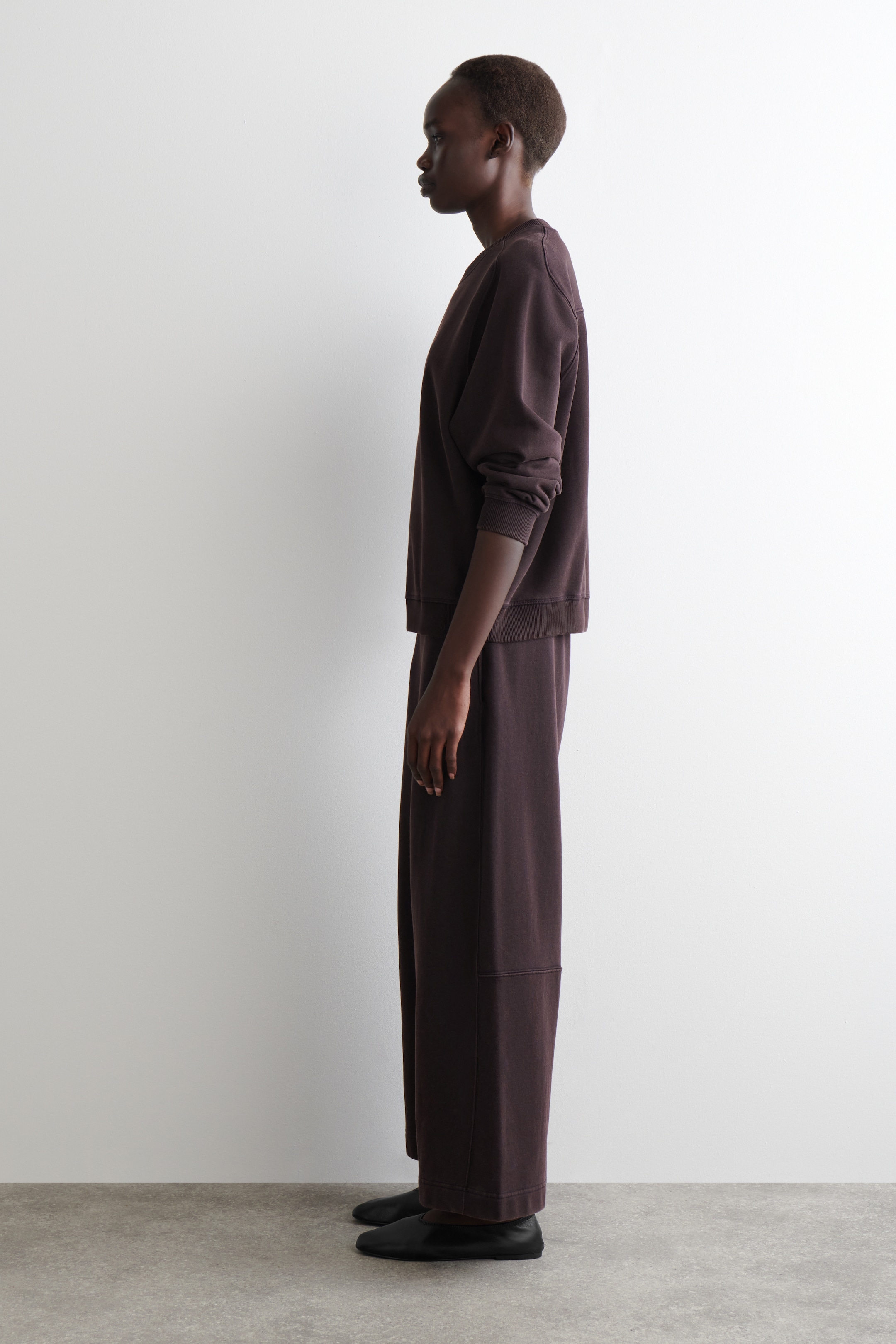 View larger image: A dark brown coordinated set is appearing on a person facing left. The set's sweatshirt is featuring dropped shoulders and ribbed cuffs, and its wide-leg joggers are displaying a cropped length with a horizontal seam on the lower leg.