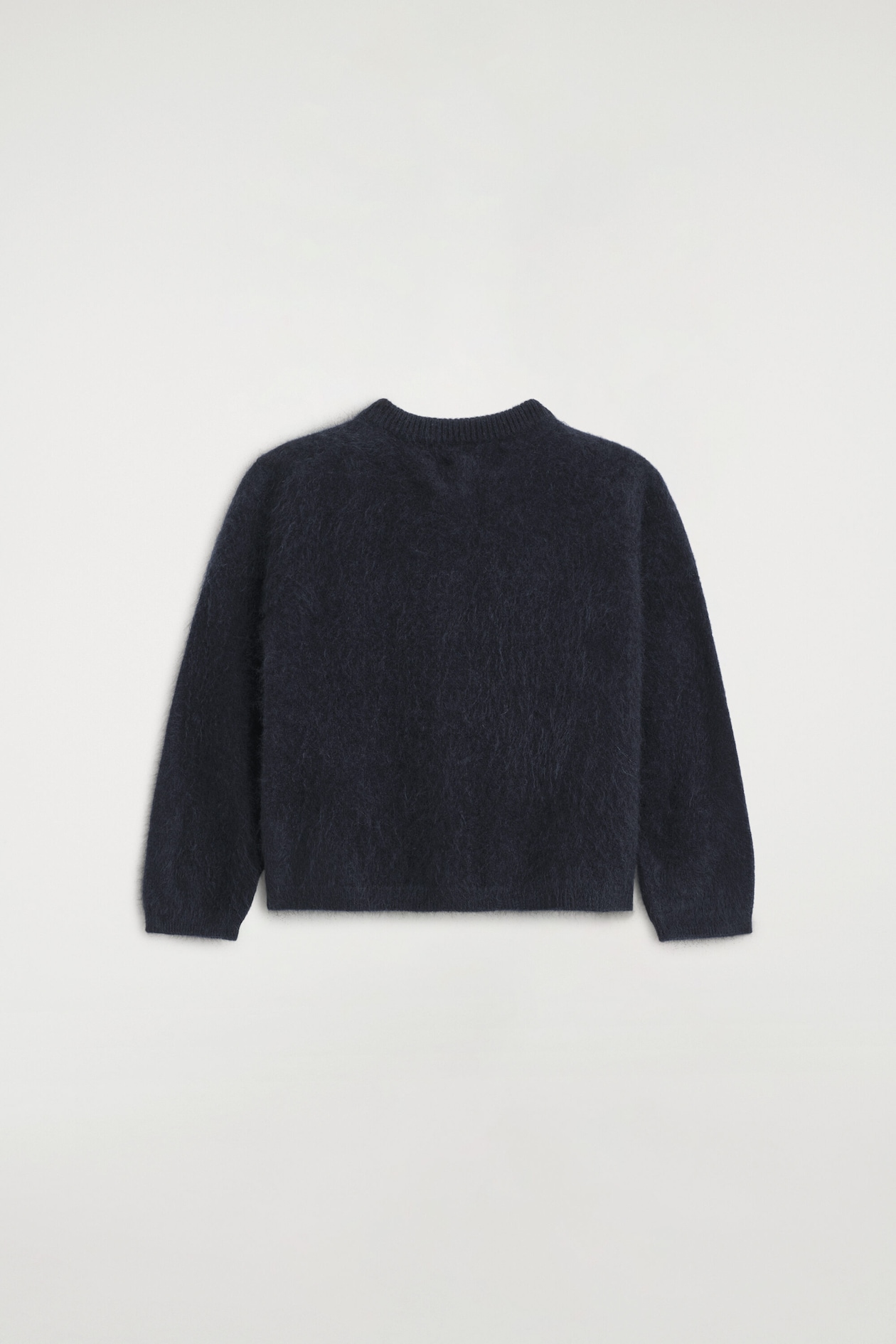 The kids’ brushed pure cashmere cardigan is shown from the back, showcasing a dark navy, fuzzy brushed texture. It features a ribbed crew neck collar, long sleeves, and a straight hem.
