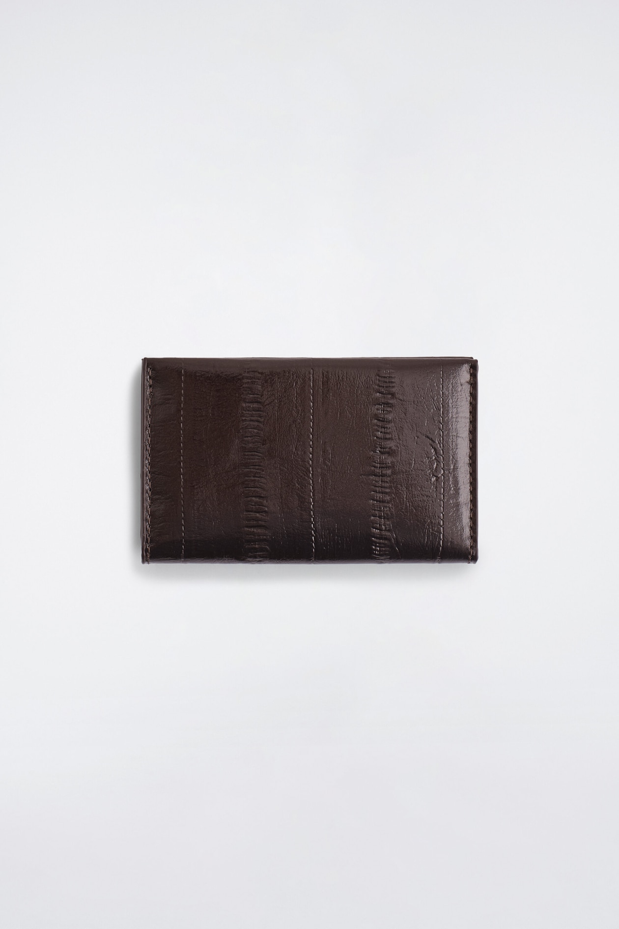 The eel-effect leather cardholder is lying flat in a front view, showcasing a dark brown glossy finish with vertical paneled stitching and textured spine-like patterns. The rectangular, folded design displays tonal topstitching along its edges and seams.