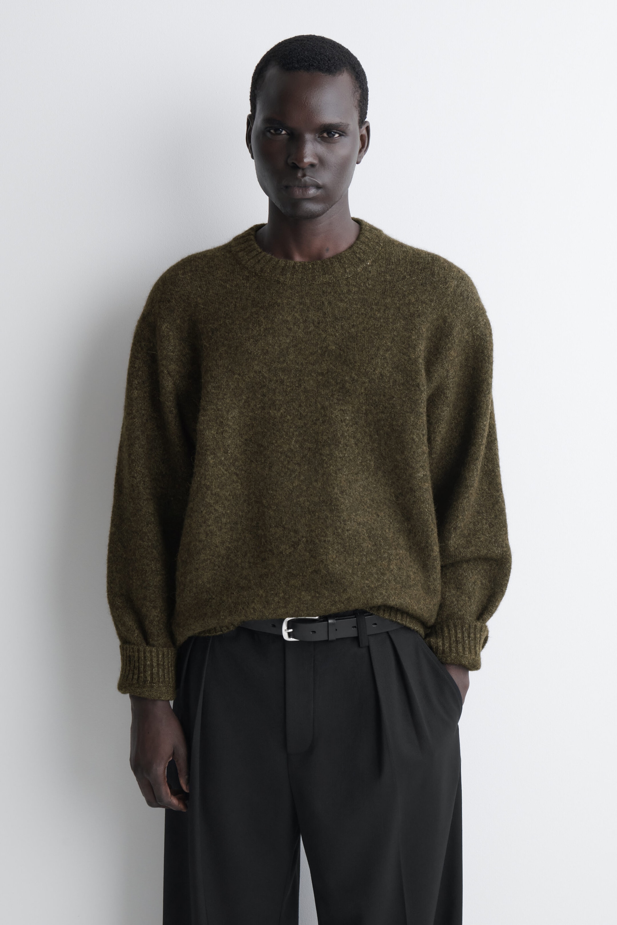 An oversized alpaca-blend crew-neck jumper in olive green is shown from the front, highlighting its fuzzy, textured knit and relaxed silhouette. The jumper features dropped shoulders, a ribbed neck, and ribbed cuffs, with the hem loosely draping over a black belt and trousers. An oversized alpaca-blend crew-neck jumper in olive green is shown from the front, highlighting its fuzzy, textured knit and relaxed silhouette. The jumper features dropped shoulders, a ribbed neck, and ribbed cuffs, with the hem loosely draping over a black belt and trousers.