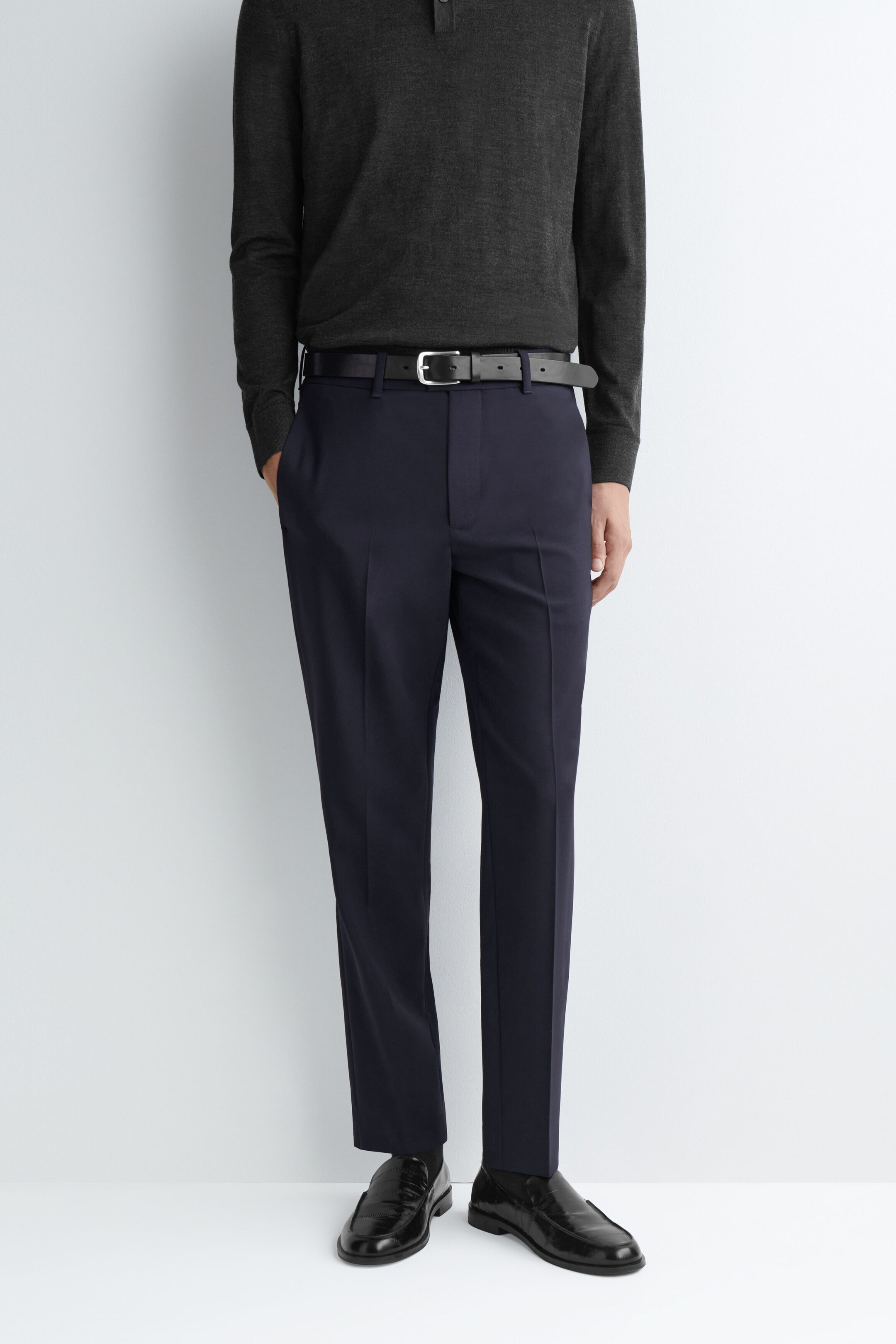 Un pantalon droit slim en laine bleu marine foncé est porté par le mannequin, associé à une ceinture en cuir noire et à un polo à manches longues en maille gris foncé rentré dans le pantalon. Le pantalon présente des plis marqués sur le devant et des poches latérales, tandis que le mannequin a une main glissée dans une poche. Un pantalon droit slim en laine bleu marine foncé est porté par le mannequin, associé à une ceinture en cuir noire et à un polo à manches longues en maille gris foncé rentré dans le pantalon. Le pantalon présente des plis marqués sur le devant et des poches latérales, tandis que le mannequin a une main glissée dans une poche.