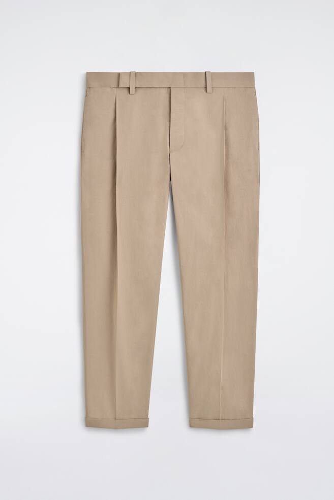 The front of beige trousers showcases a straight-leg design, featuring two prominent front pleats on each leg and belt loops along the waistband, with the hems turned up. - 1